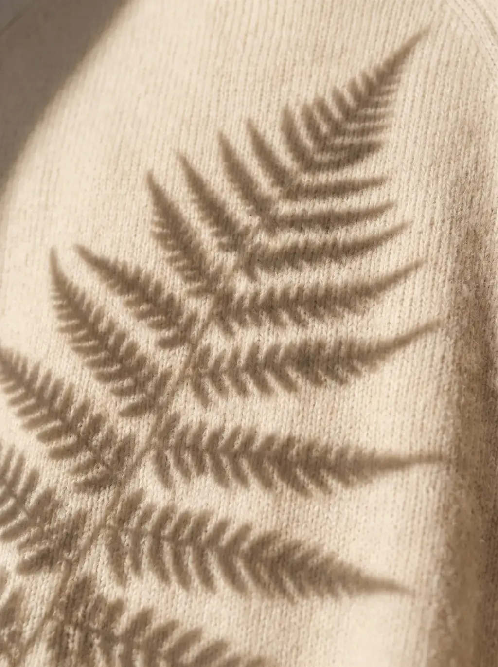 Gros plan sur un tricot crème au motif torsadé en feuille de fougère, jeu d'ombre et de lumière