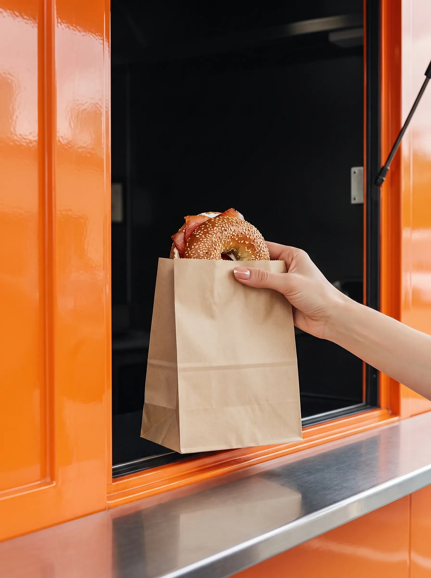 Main recevant un sac kraft avec bagel depuis la fenêtre d'un food truck orange