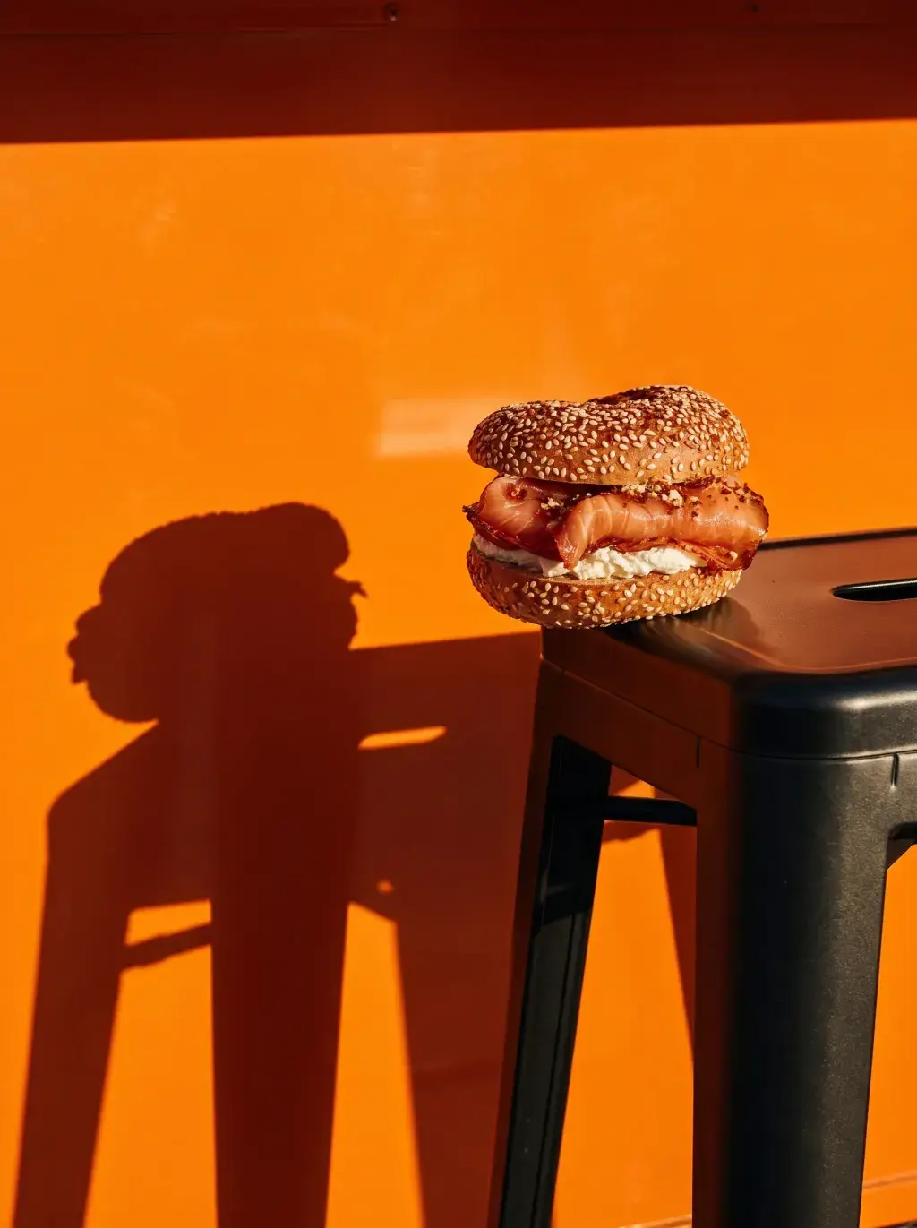Bagel saumon posé sur un tabouret noir devant un food truck orange avec ombre portée