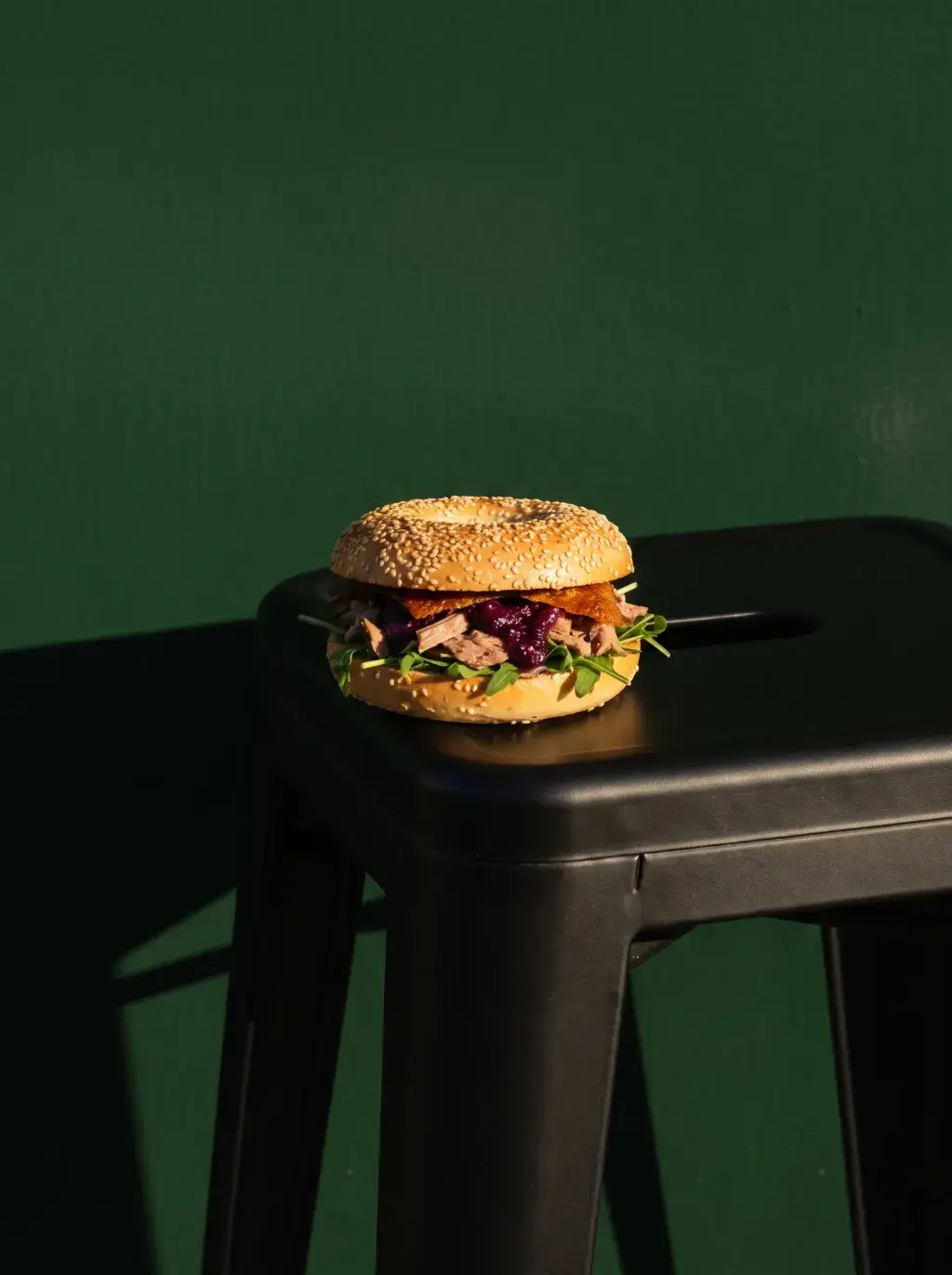 Bagel pulled pork chou rouge roquette posé sur un tabouret noir devant fond vert sombre