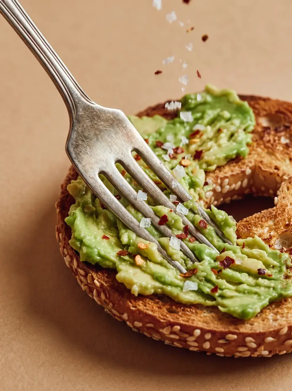 Fourchette écrasant de l'avocat sur une moitié de bagel toasté avec sel et flocons de piment