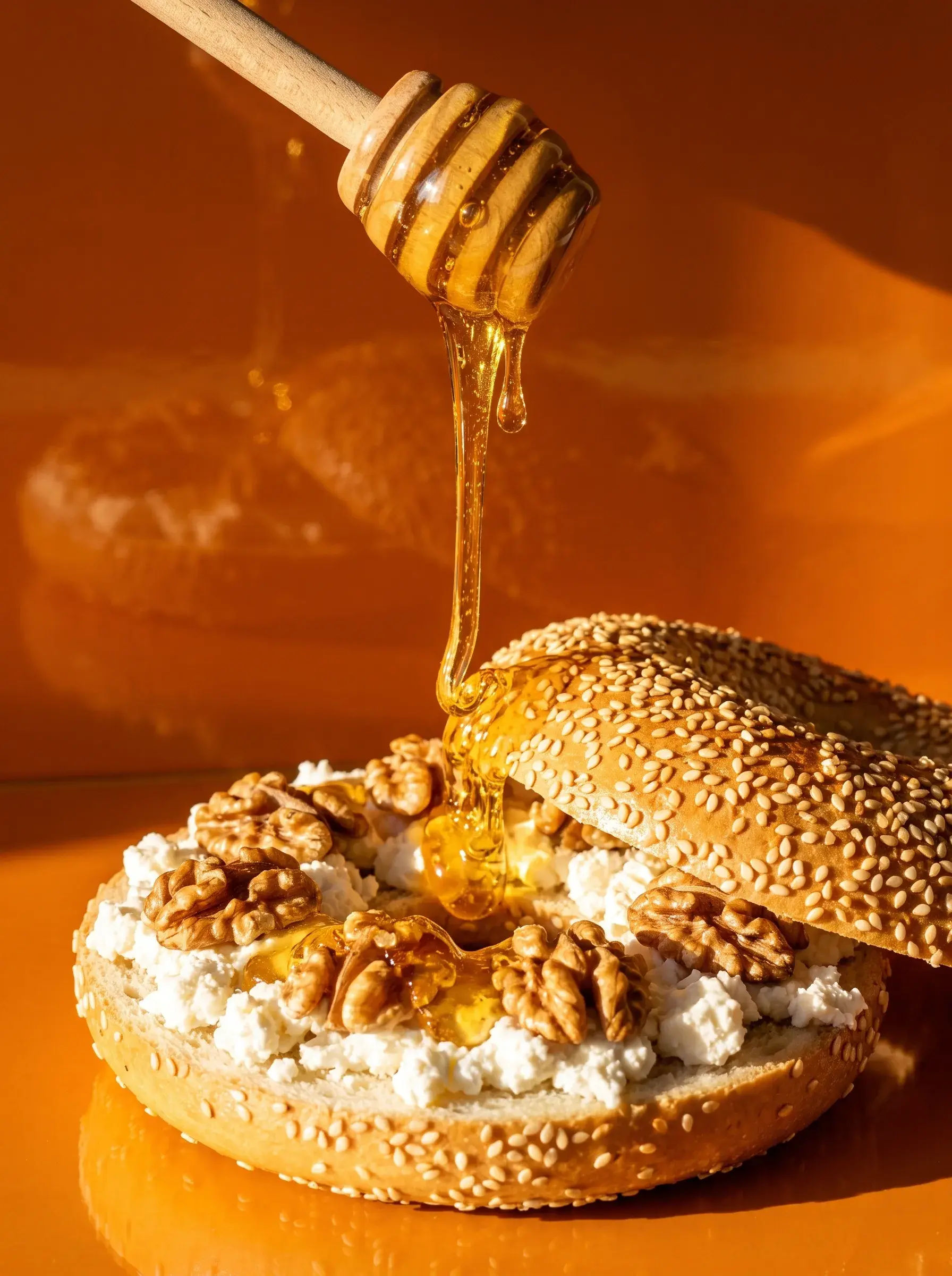 Filet de miel coulant d'un dipper sur un bagel ricotta noix sur fond orange doré