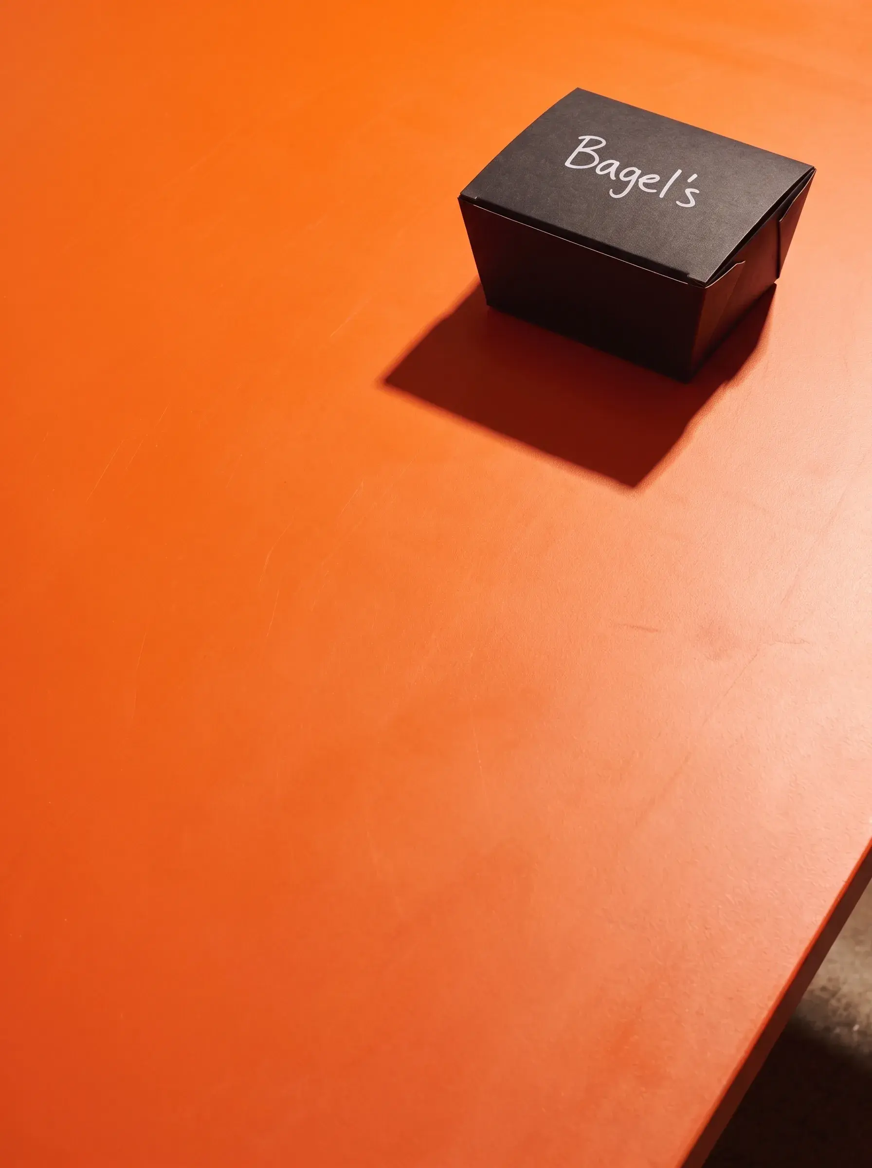 Boîte noire rectangulaire Bagel's fermée sur table orange avec ombre portée composition épurée