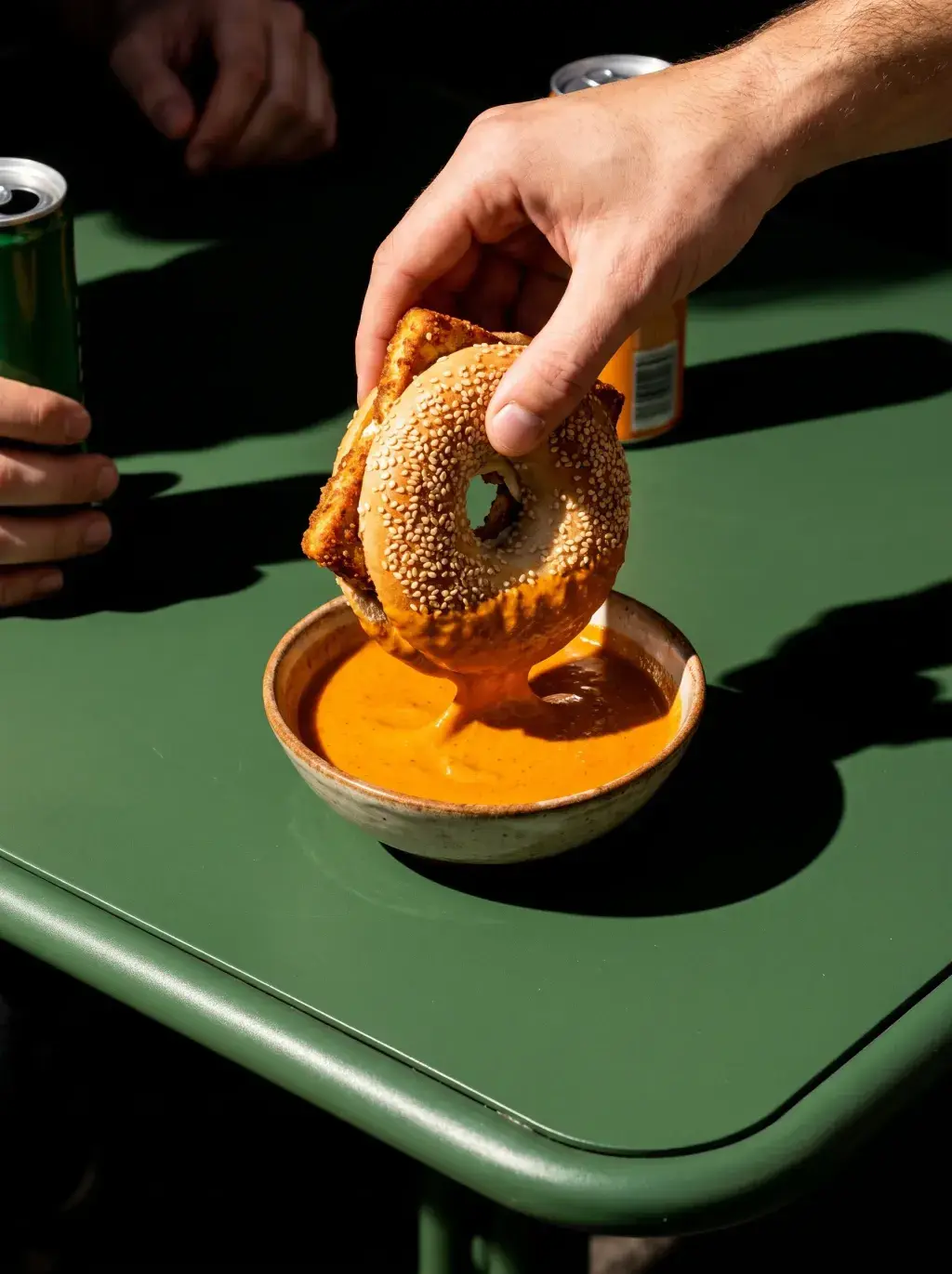 Main trempant un bagel au sésame dans une sauce curry sur table verte de bistrot