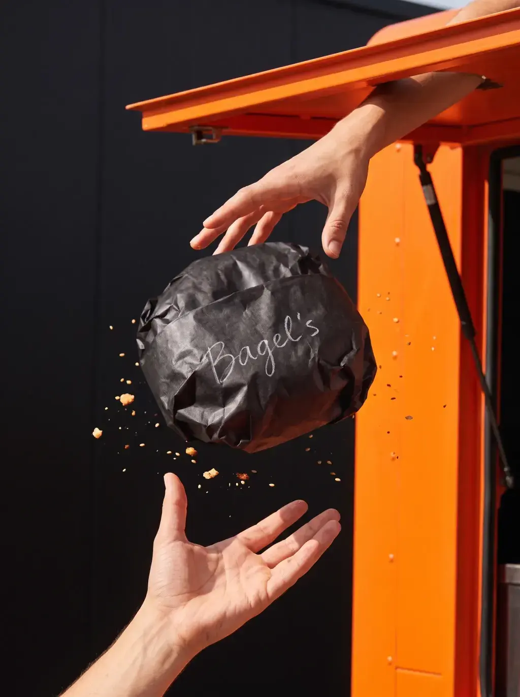 Passation d'un sac Bagel's depuis le food truck orange vers une main tendue, fond noir
