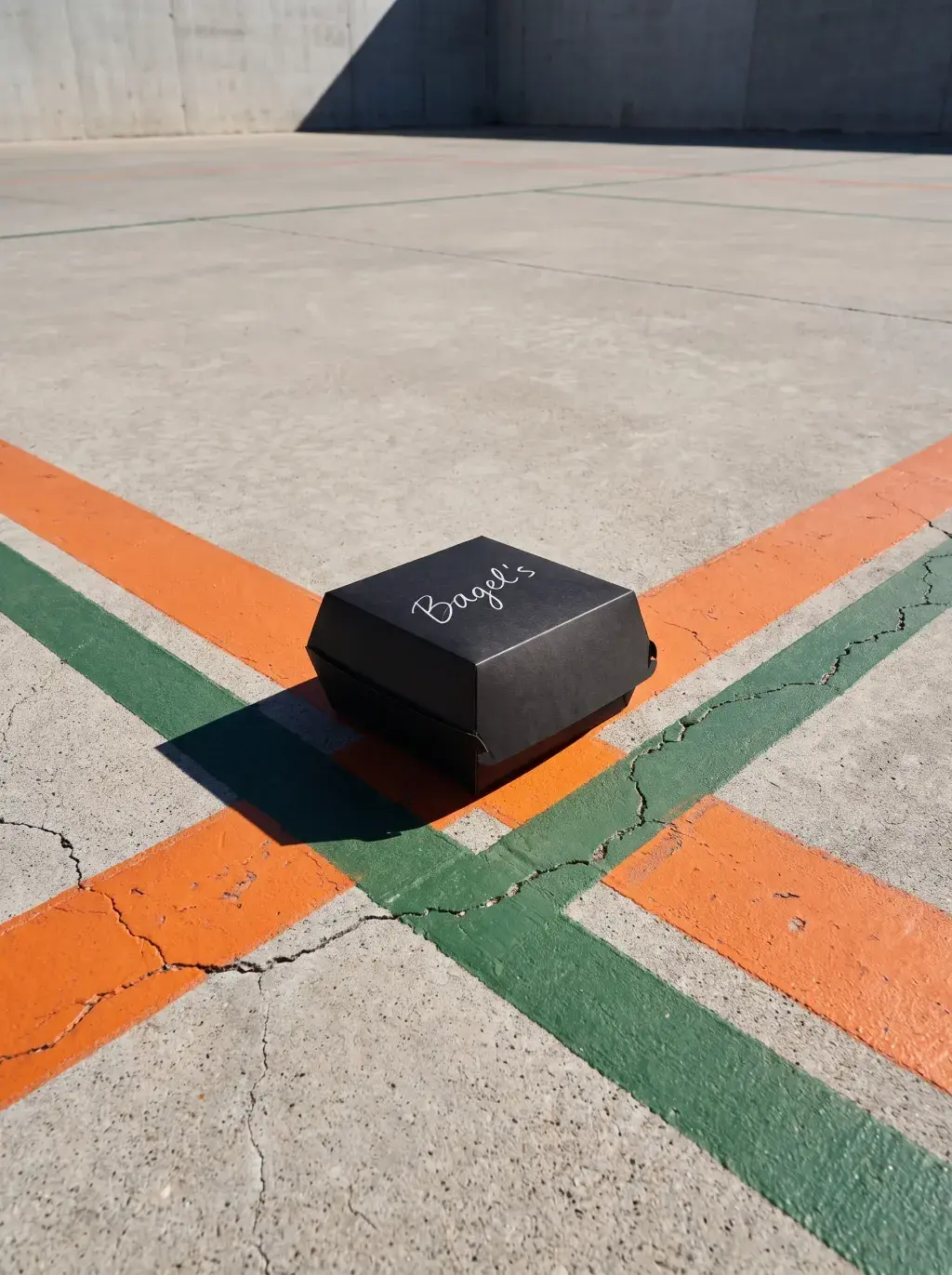 Boîte noire Bagel's sur sol béton avec lignes orange et vertes et mur derrière