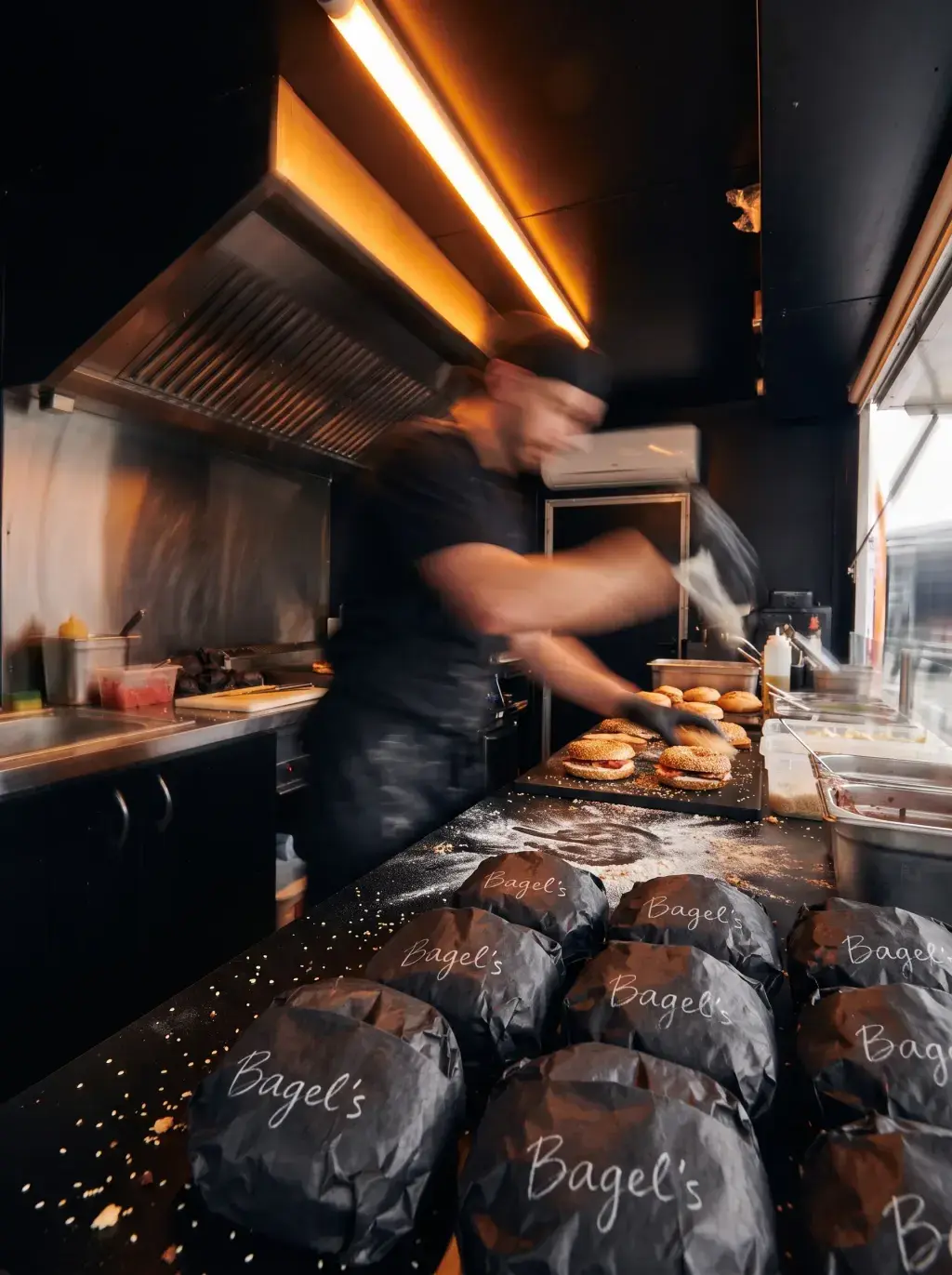 Cuisinier en mouvement flou dans la cuisine du food truck avec rangées de sacs Bagel's prêts