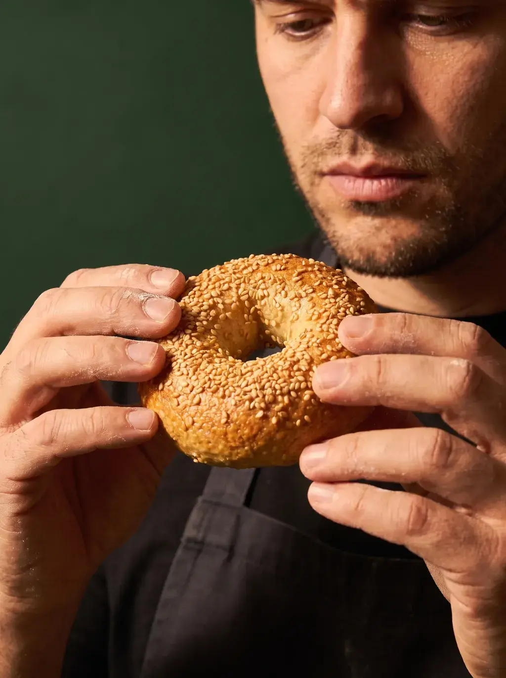 Boulanger tenant un bagel au sésame doré cuit entre ses mains sur fond vert