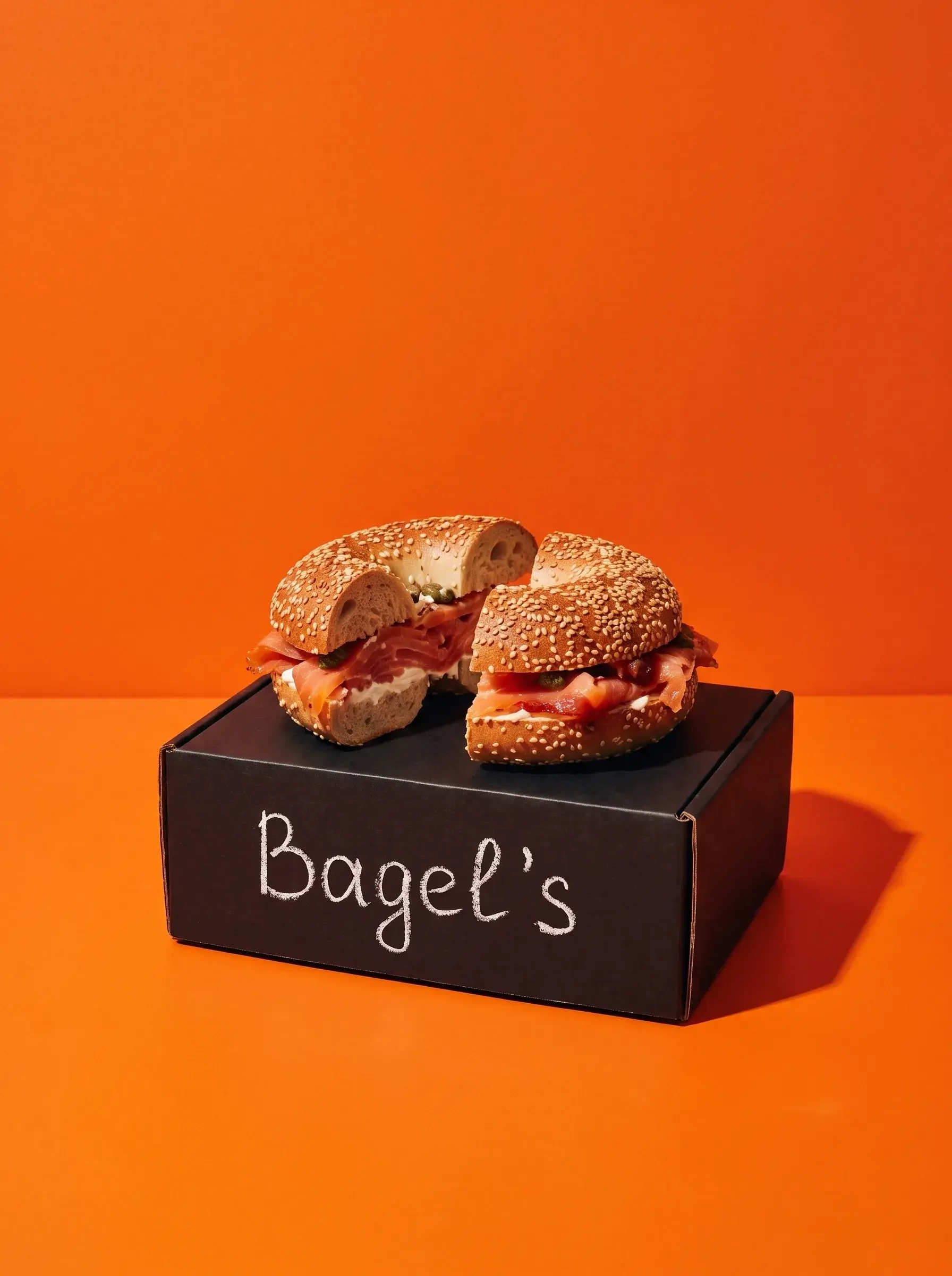 Bagel saumon cream cheese coupé en deux posé sur une boîte Bagel's noire, fond orange