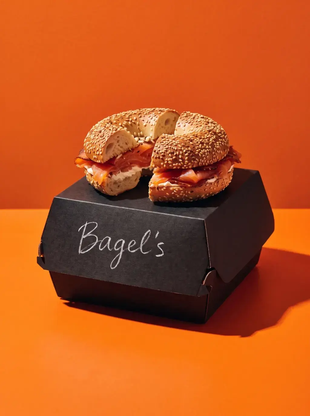 Bagel saumon cream cheese coupé en deux sur une boîte Bagel's noire sur fond orange vif