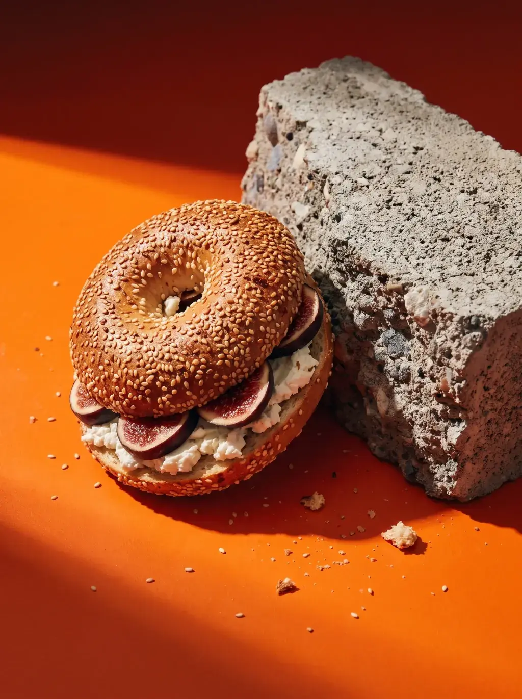 Bagel à la figue et cream cheese contre un bloc de béton brut sur fond orange vif