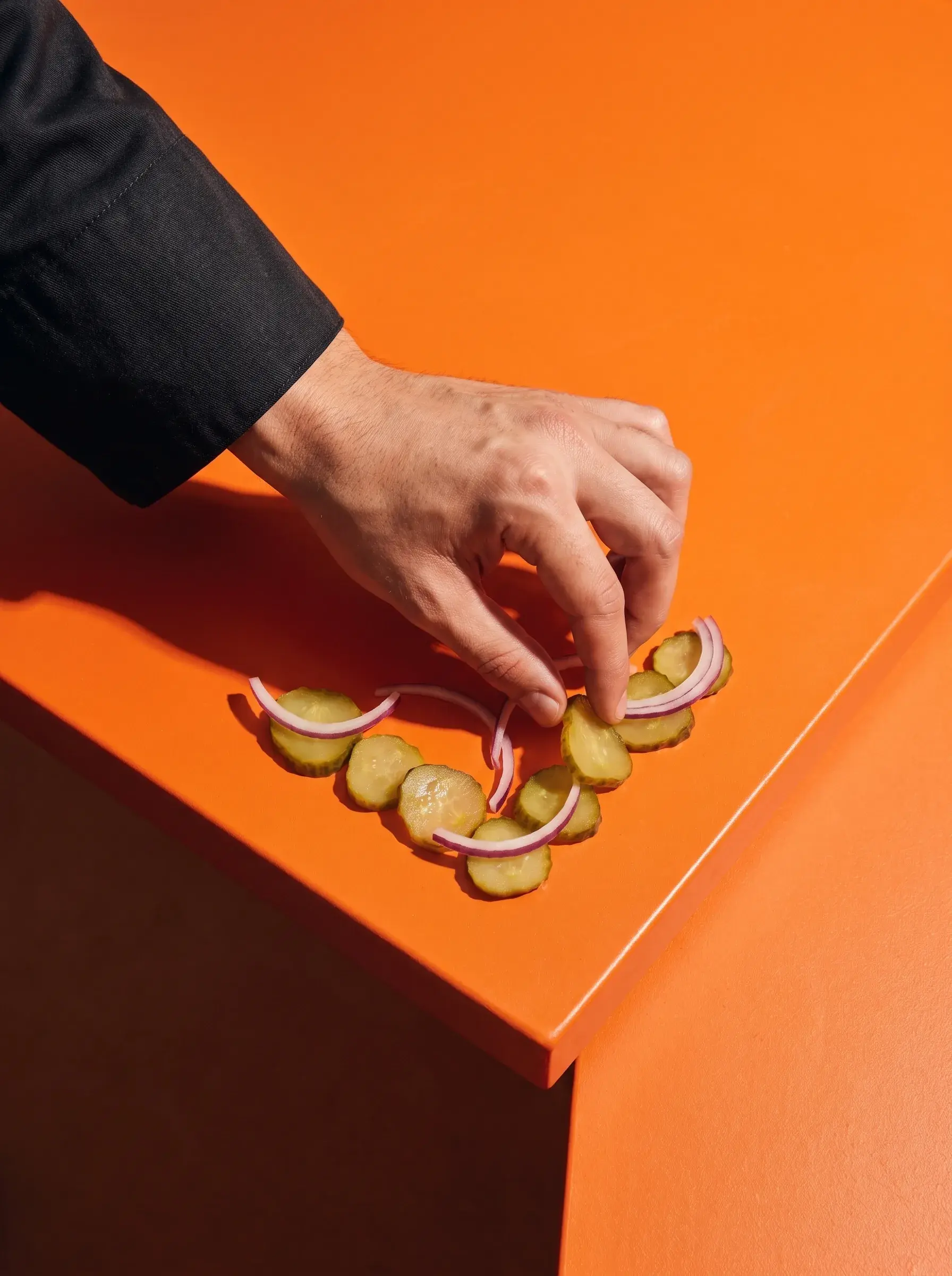 Main arrangeant des rondelles de cornichon et d'oignon rouge en forme de cœur sur fond orange