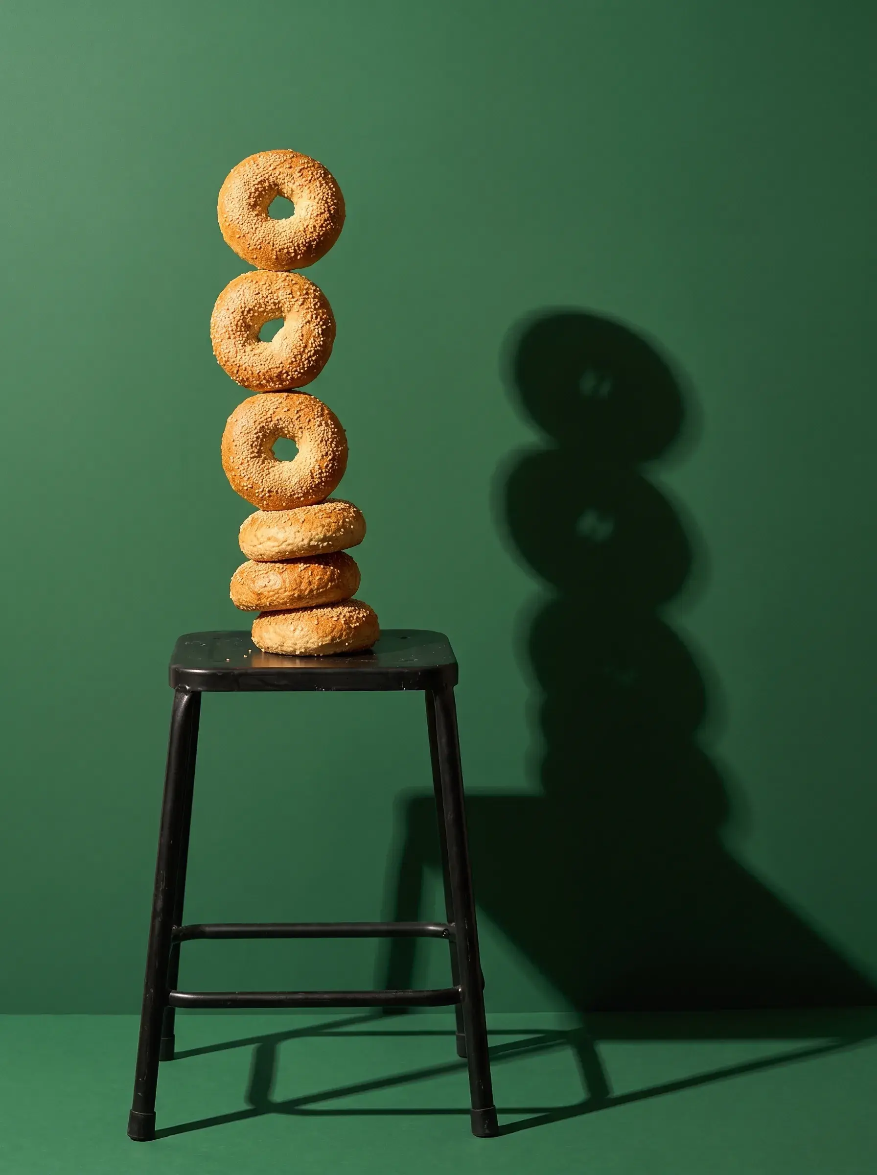Tour de cinq bagels au sésame en équilibre sur un tabouret noir sur fond vert