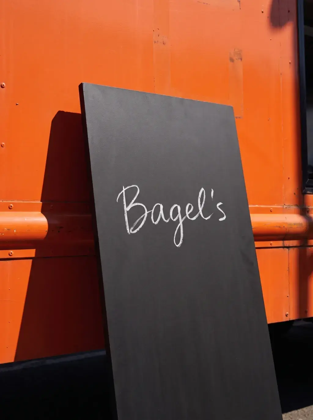Grande ardoise noire Bagel's appuyée contre le flanc du food truck orange