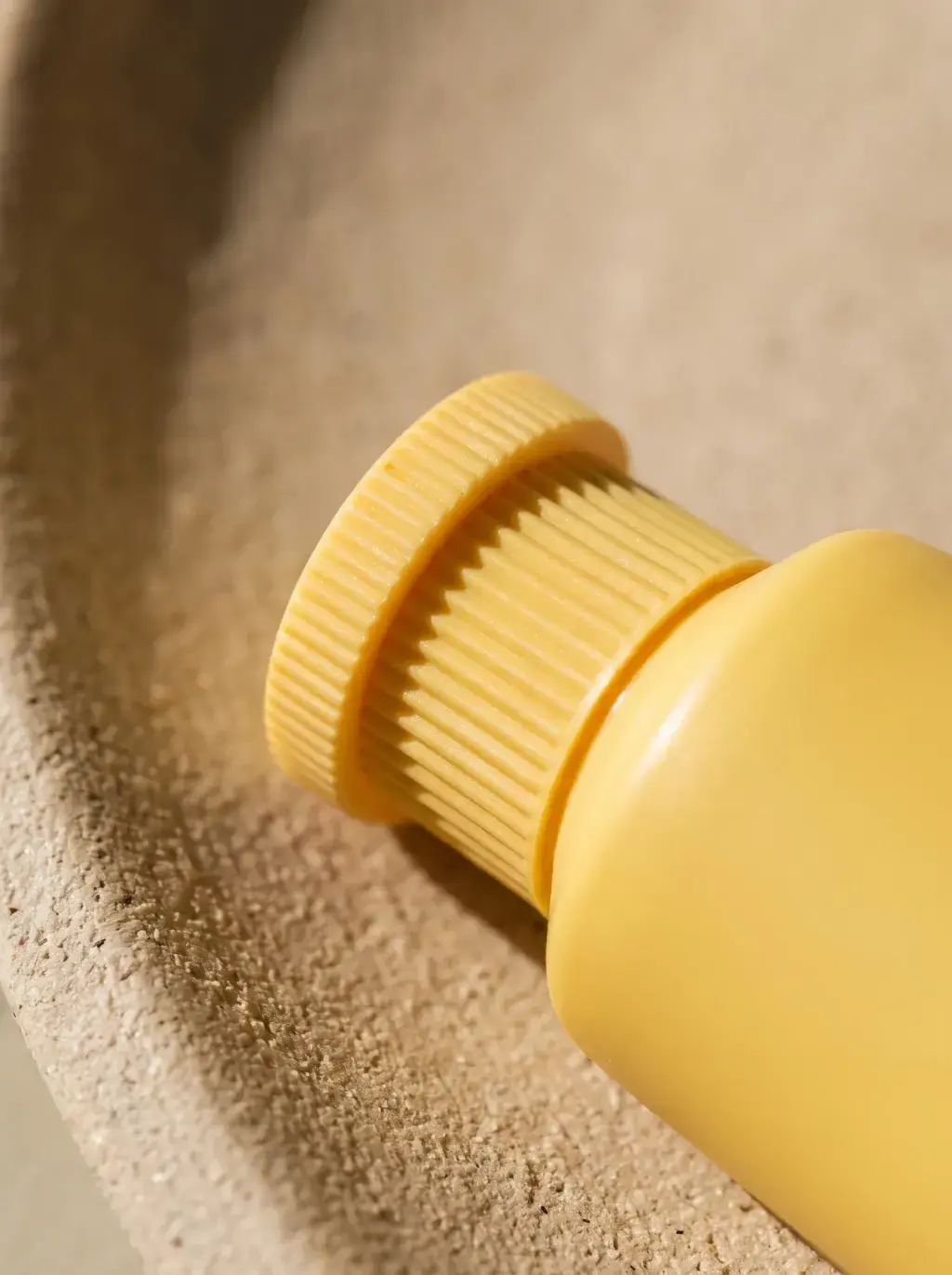 Macro du bouchon strié d’un tube cosmétique jaune posé sur un textile beige