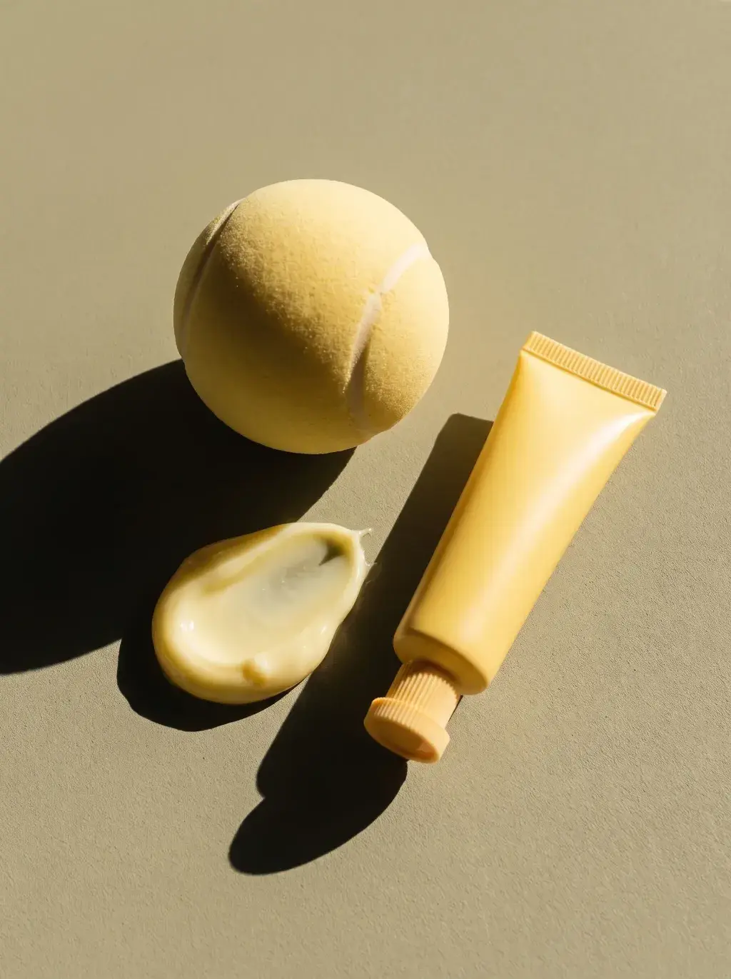 Tube jaune, balle de tennis et noisette de crème composés sur fond vert olive