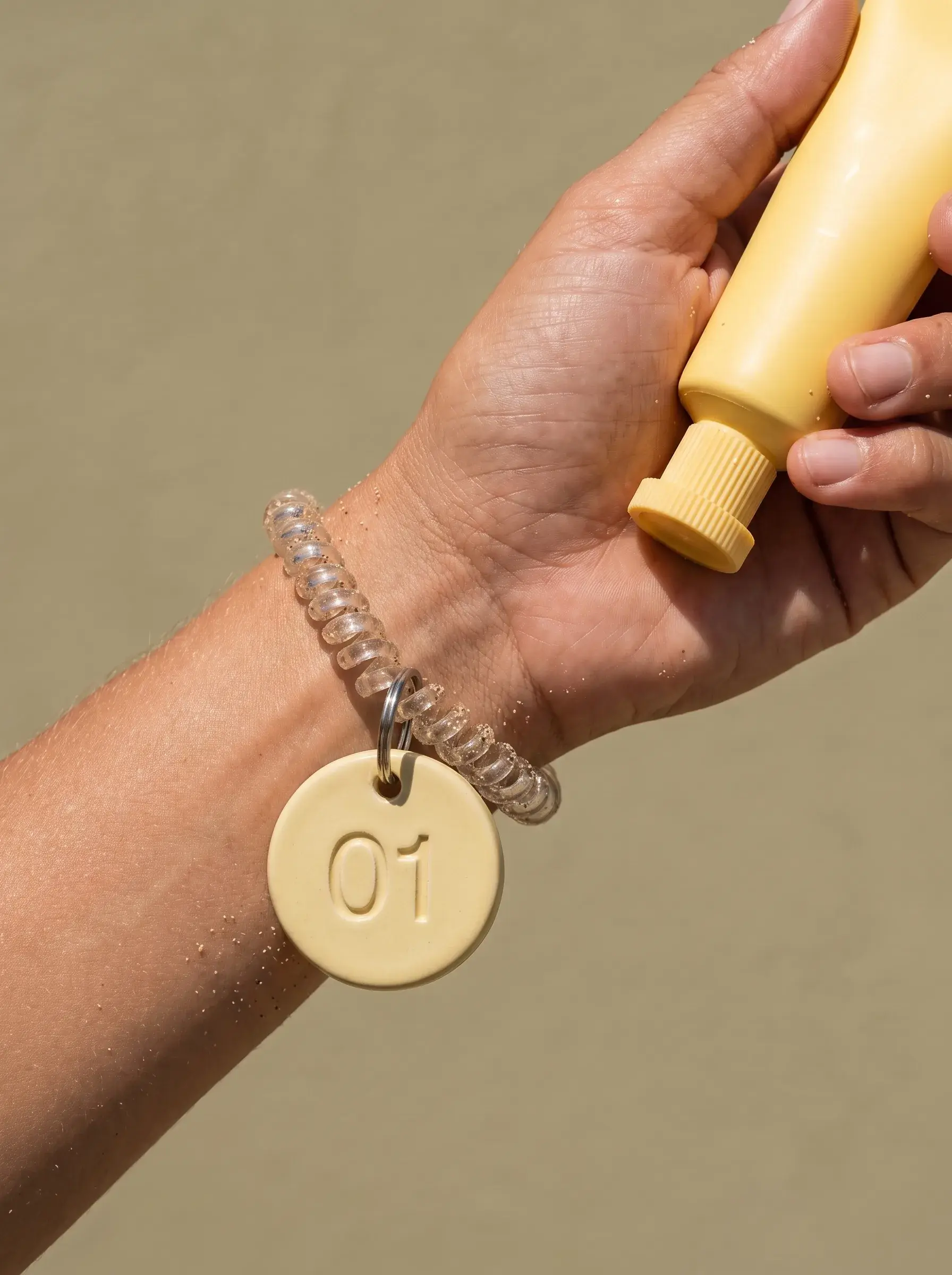 Main tenant un tube jaune au-dessus d’un bracelet avec médaillon féminin