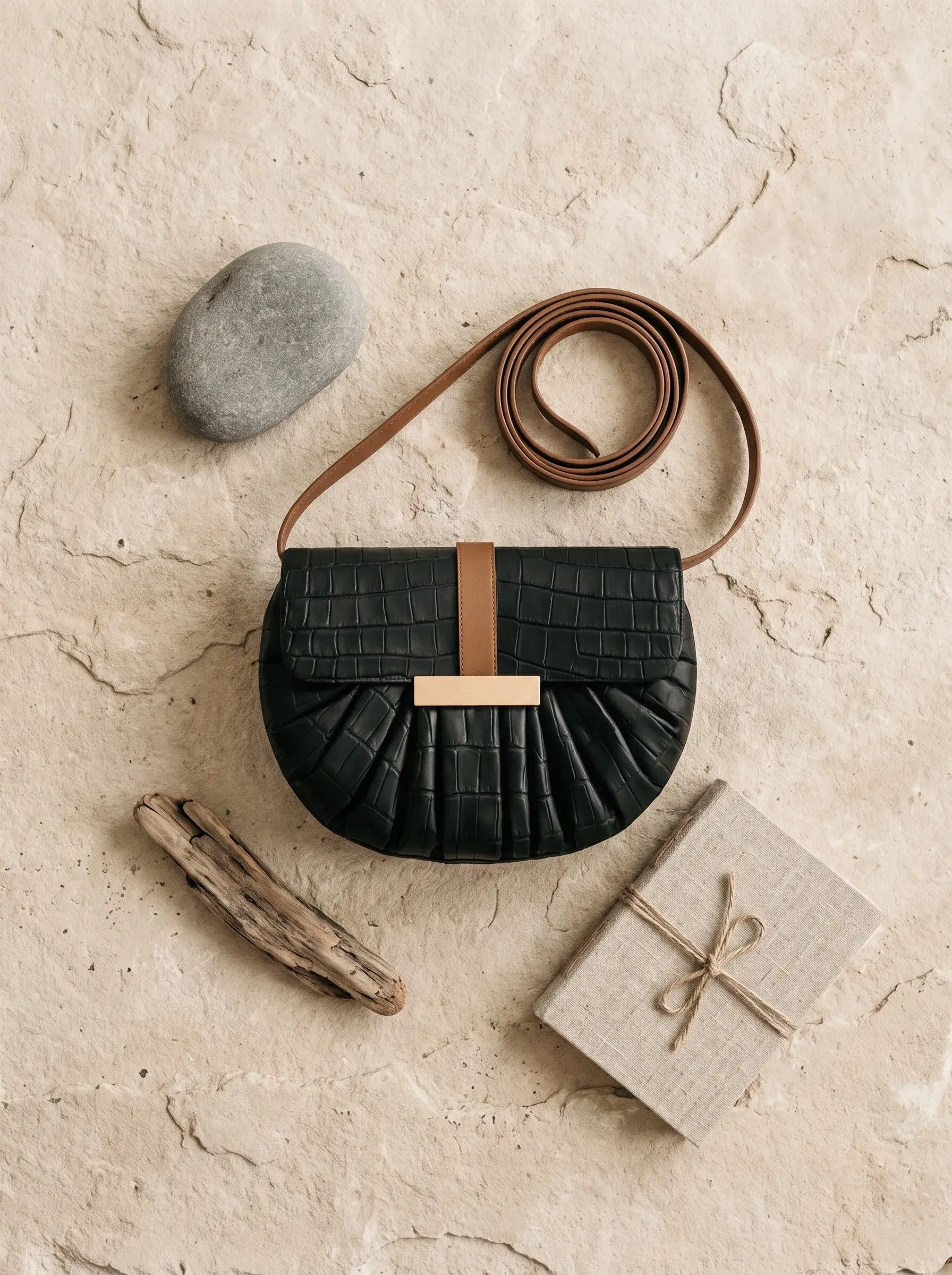 Sac noir, sangle brune et outils composés à plat sur un sol minéral