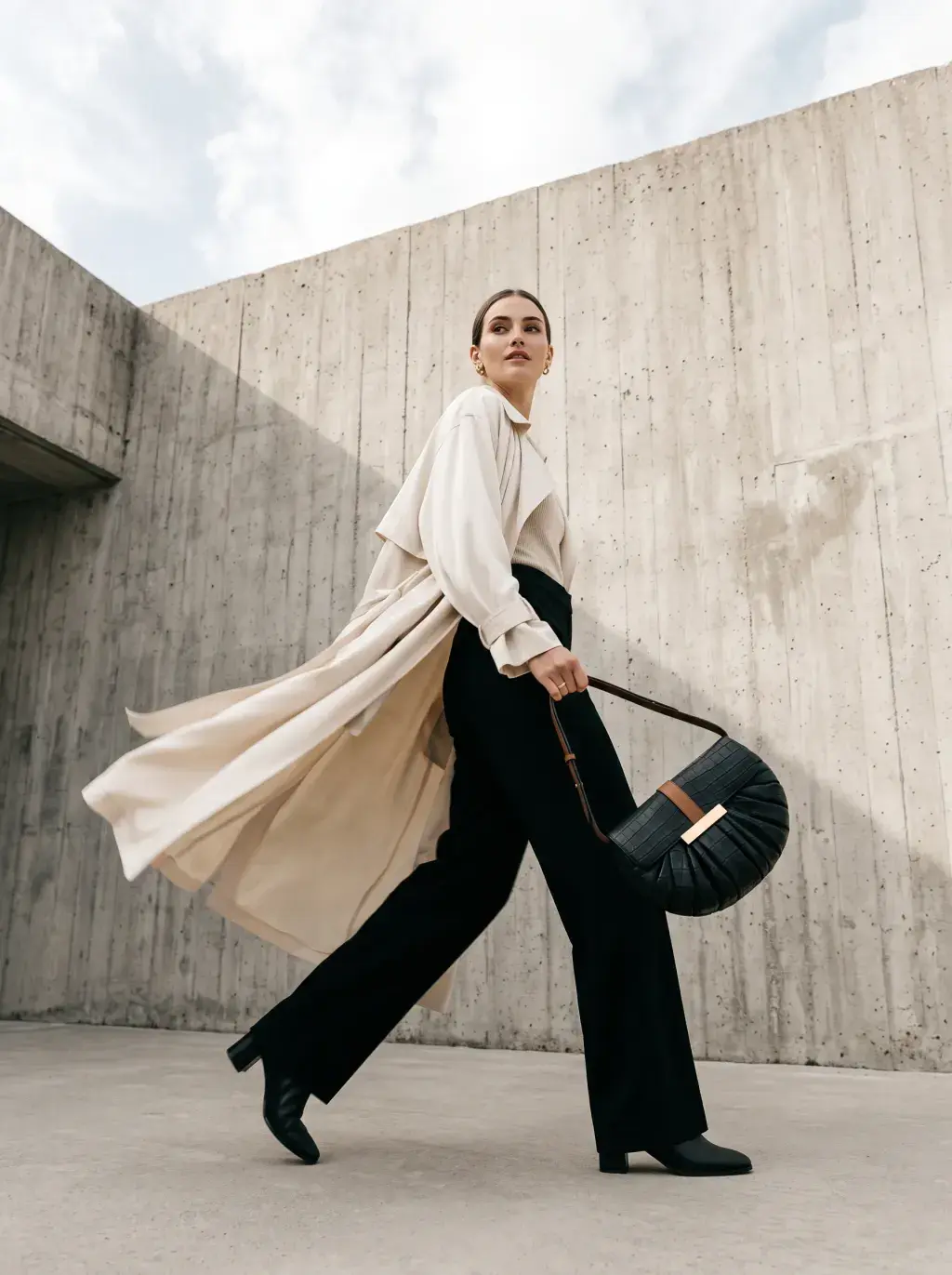 Femme en tenue noire et manteau blanc marchant avec un sac bandoulière tressé