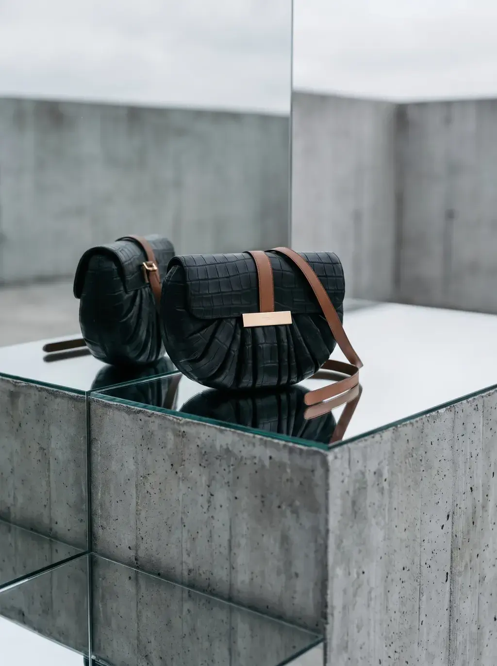 Deux sacs noirs réfléchis sur un plateau miroir au milieu d’une architecture de béton