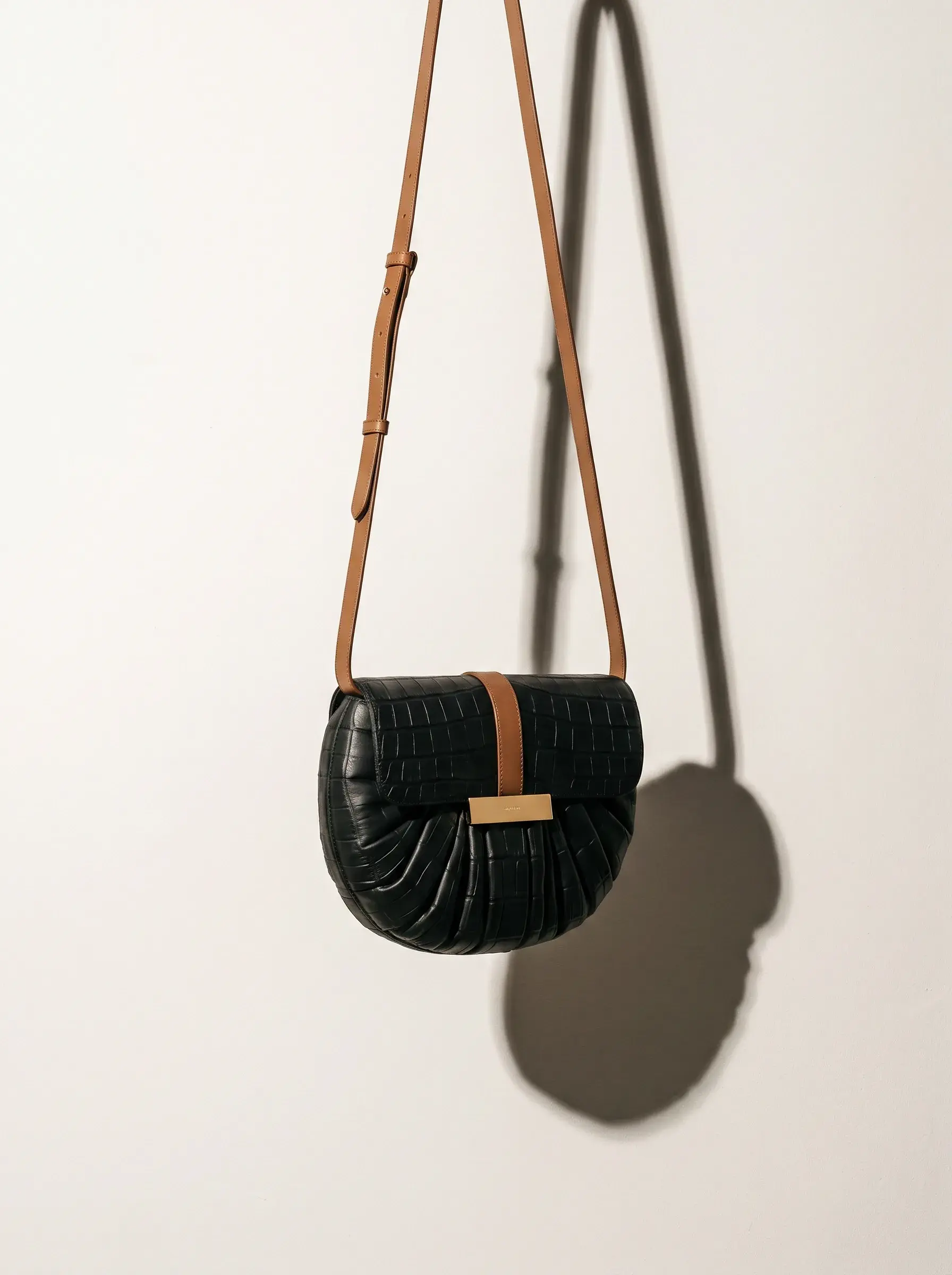 Petit sac noir suspendu seul à un mur blanc par sa longue bandoulière