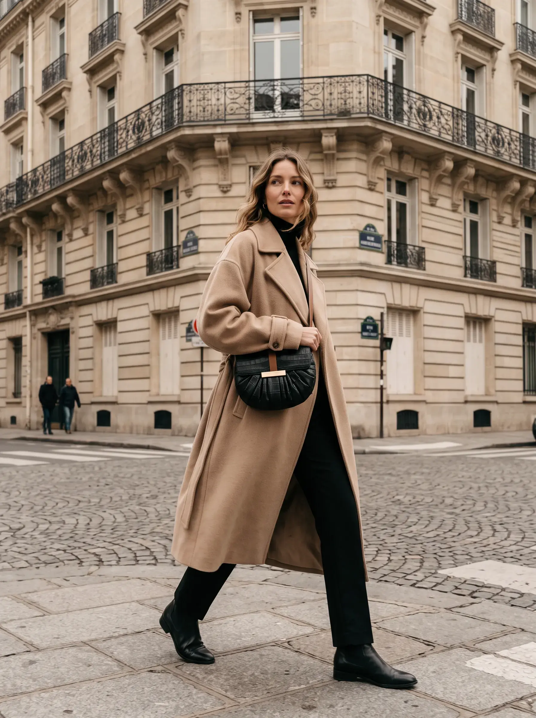 Femme en manteau camel marchant avec un sac noir sur une place parisienne