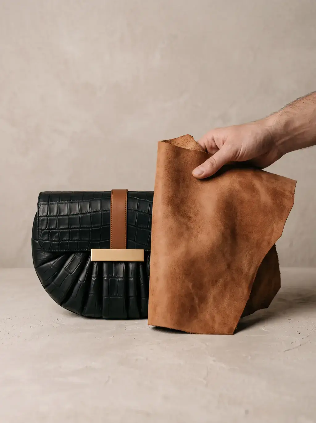 Main présentant une grande pièce de cuir brun à côté d’un sac noir