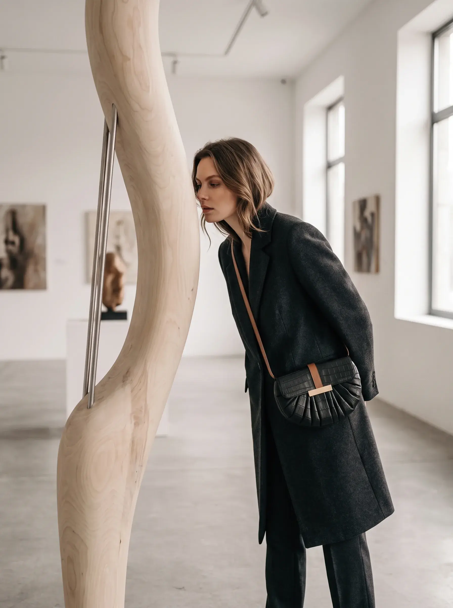 Femme en manteau noir portant un sac tressé dans une galerie de sculptures