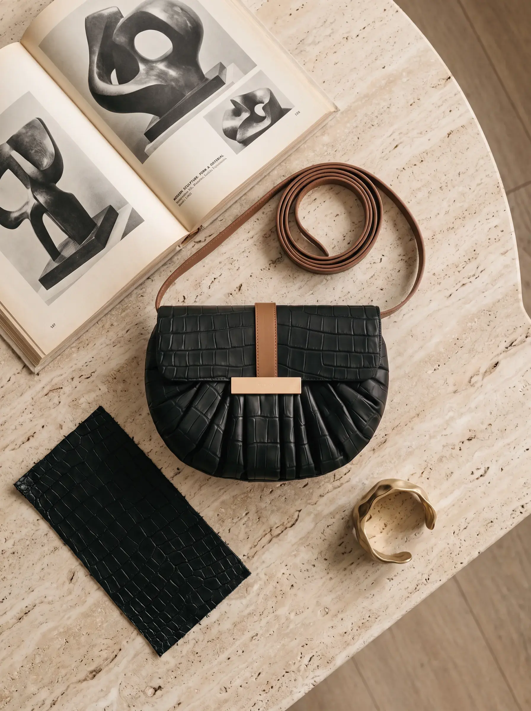 Sac noir, livre d’art et sangle brune disposés sur une table claire