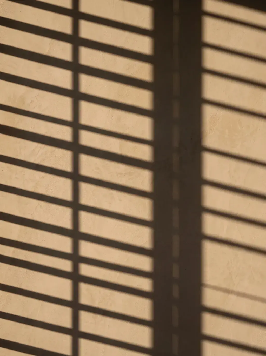 Ombres régulières de stores projetées sur un mur beige
