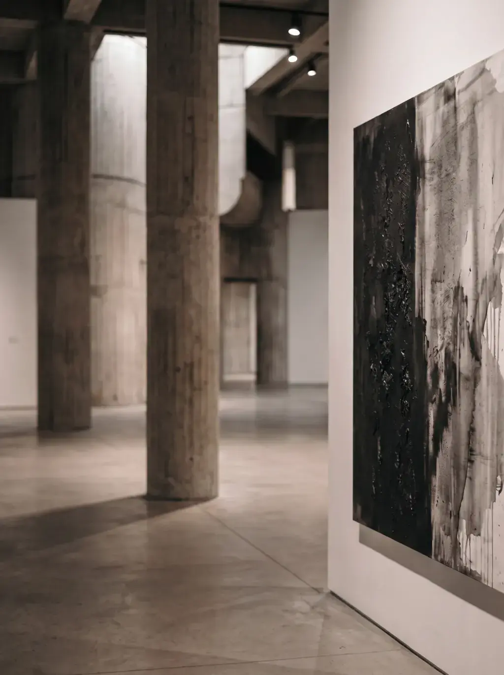 Galerie brutaliste vide aux colonnes de béton et grande toile abstraite