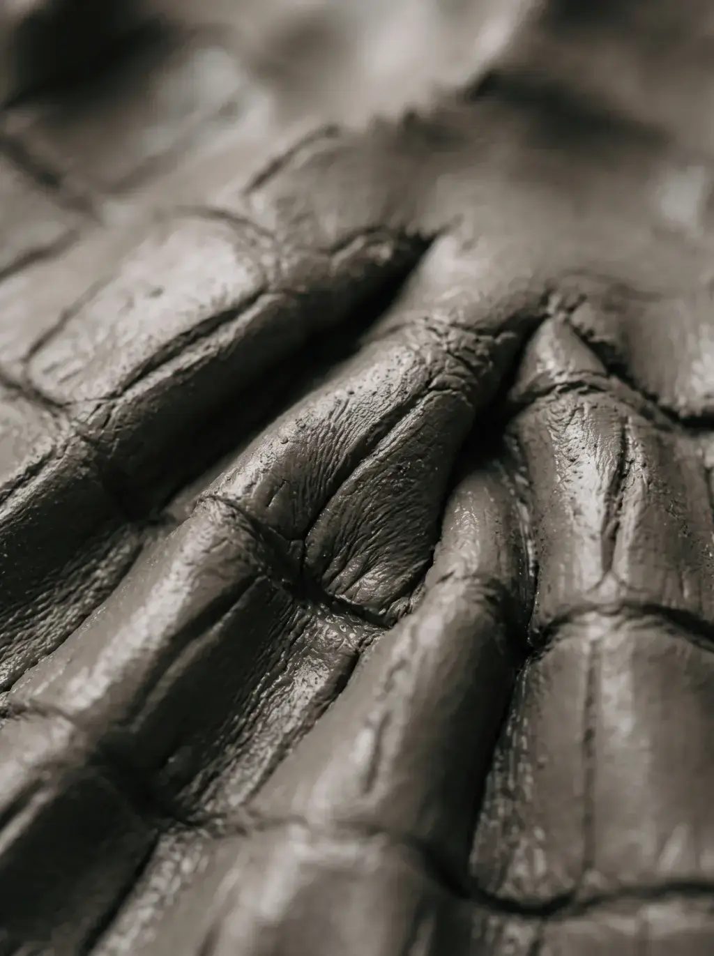 Macro d’un cuir noir plissé aux reflets métalliques et coutures profondes