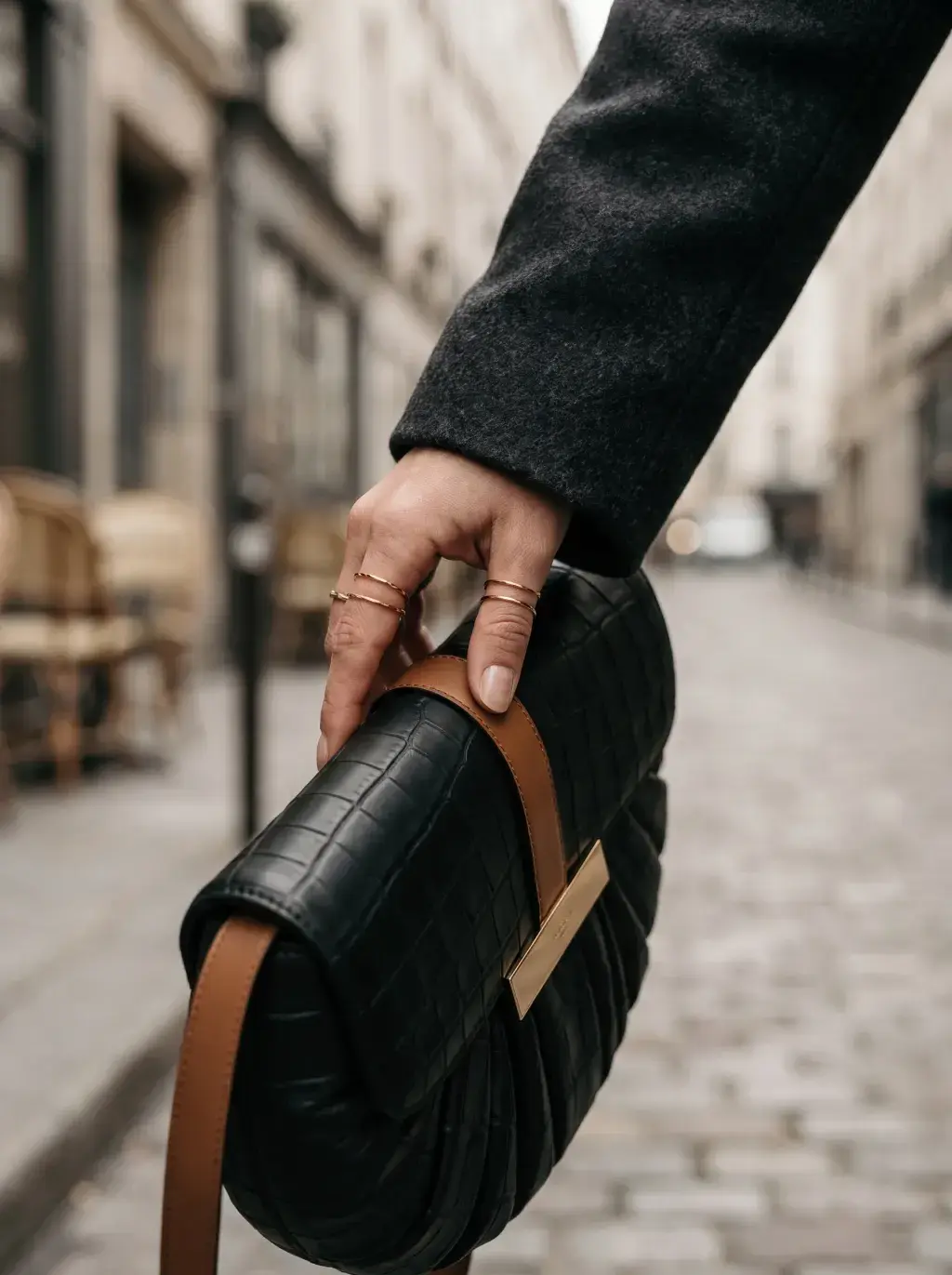 Main tenant un sac noir plissé par sa large sangle brune dans une rue