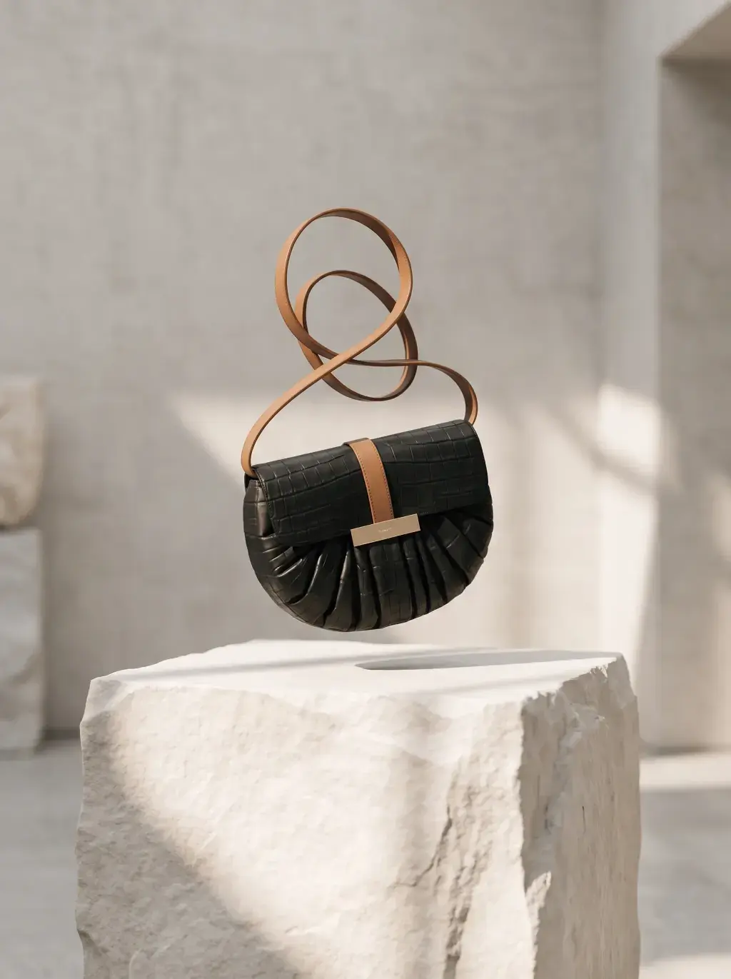 Petit sac noir à bandoulière formant une boucle au-dessus d’un socle blanc