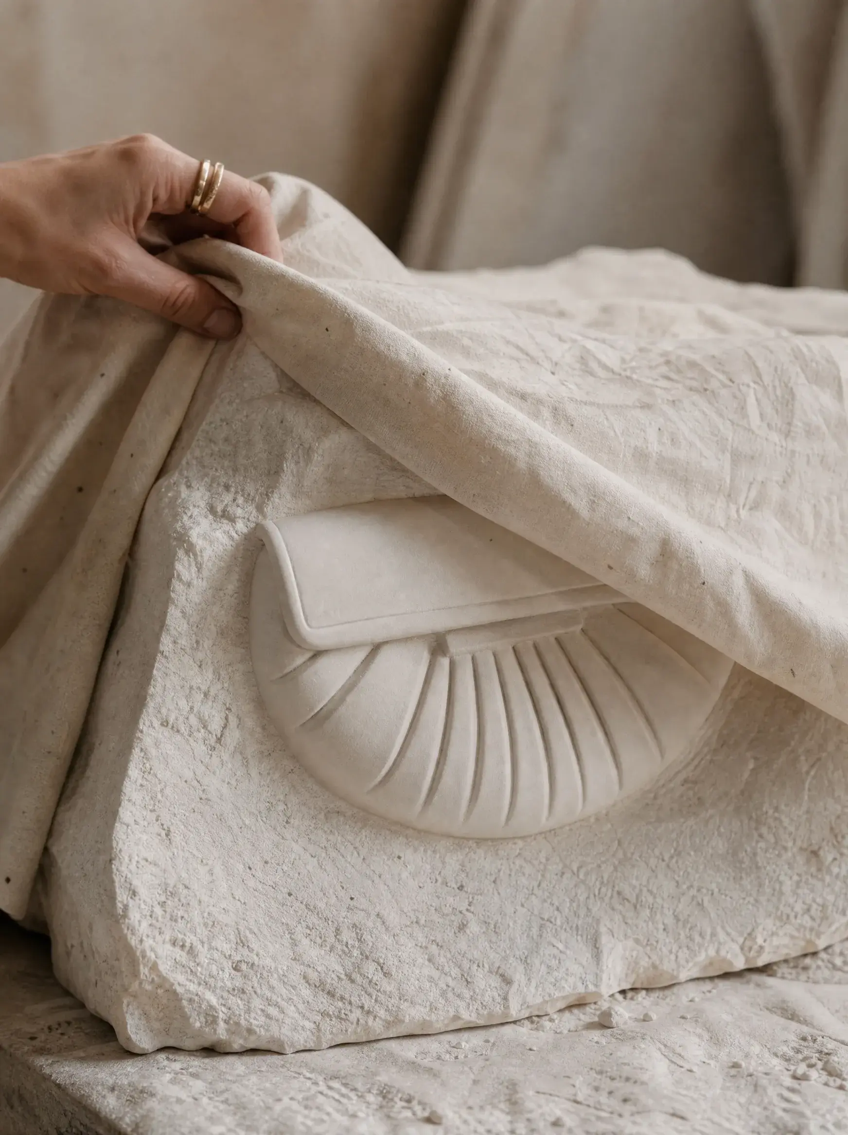 Main soulevant une toile blanche pour révéler un prototype de sac sculpté