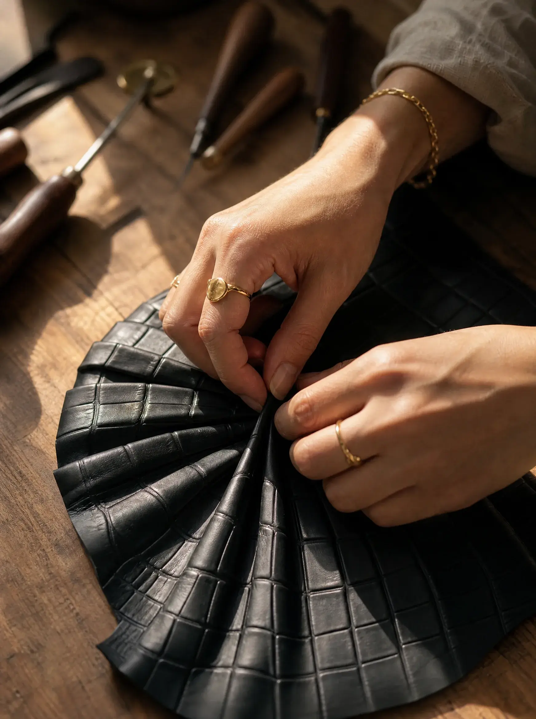 Mains d’artisane assemblant les plis d’un sac en cuir noir sur un établi