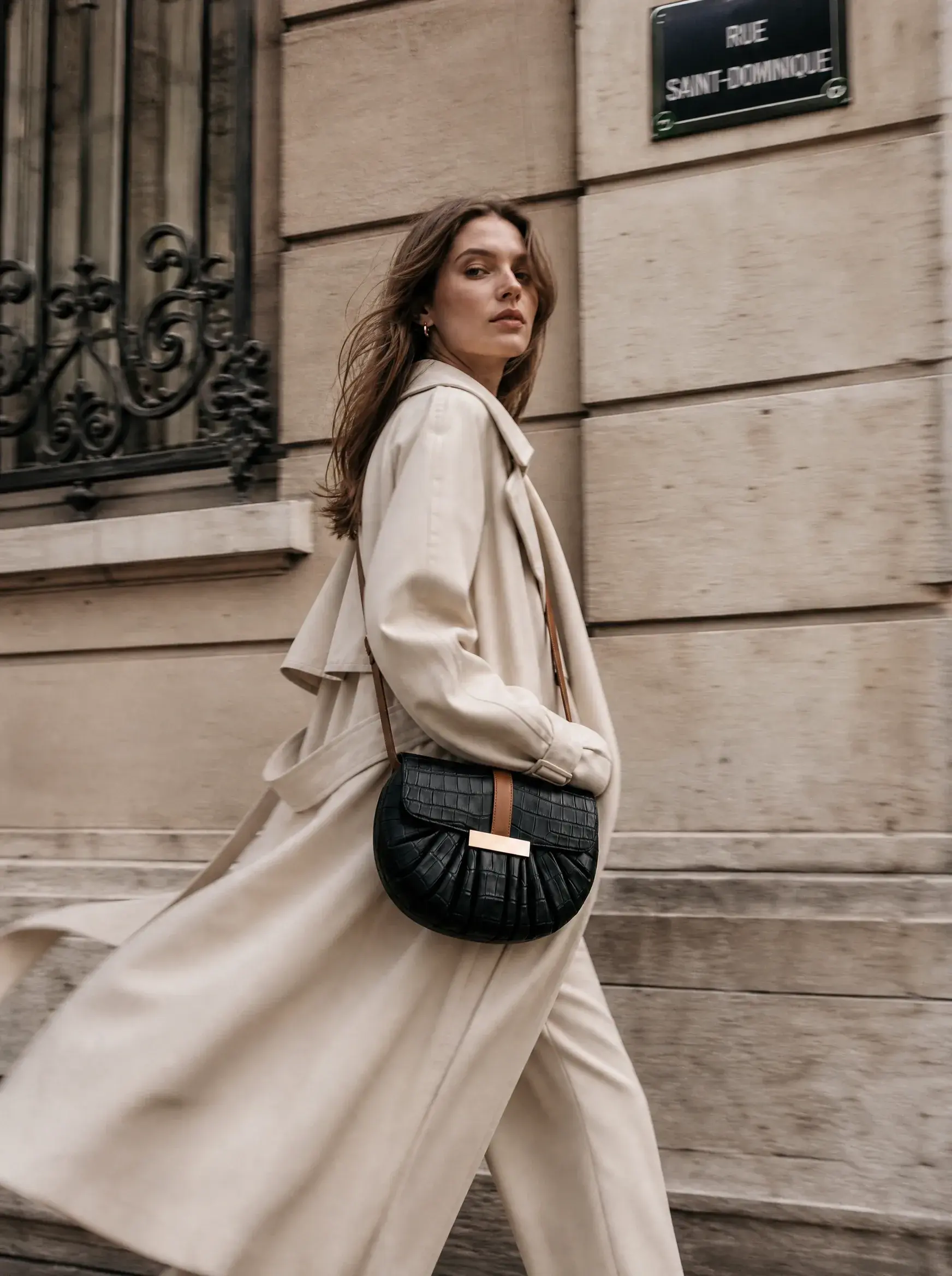 Femme en trench blanc portant un sac noir dans une rue parisienne