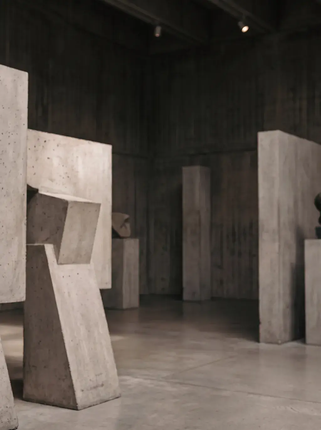Sculptures abstraites en béton et pierre dans galerie sombre et dramatique