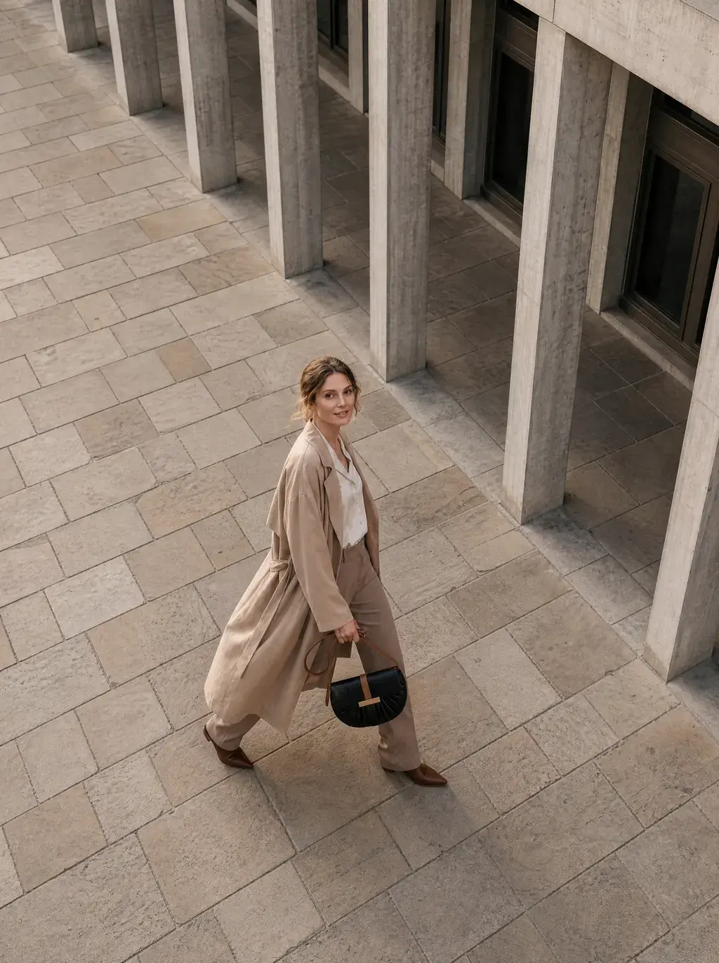 Vue aérienne — femme en trench beige marchant le long d'une colonnade béton