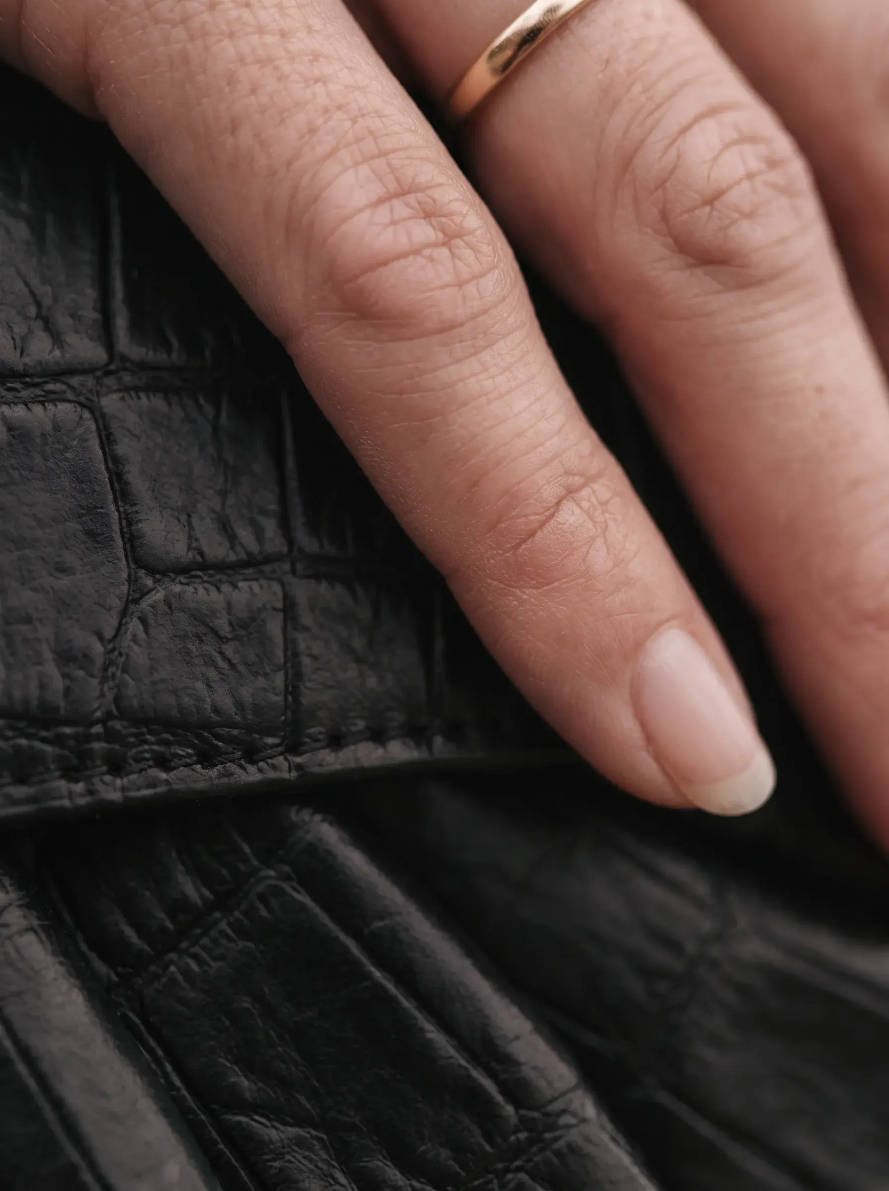 Doigts posés sur les plis souples d’un sac en cuir noir