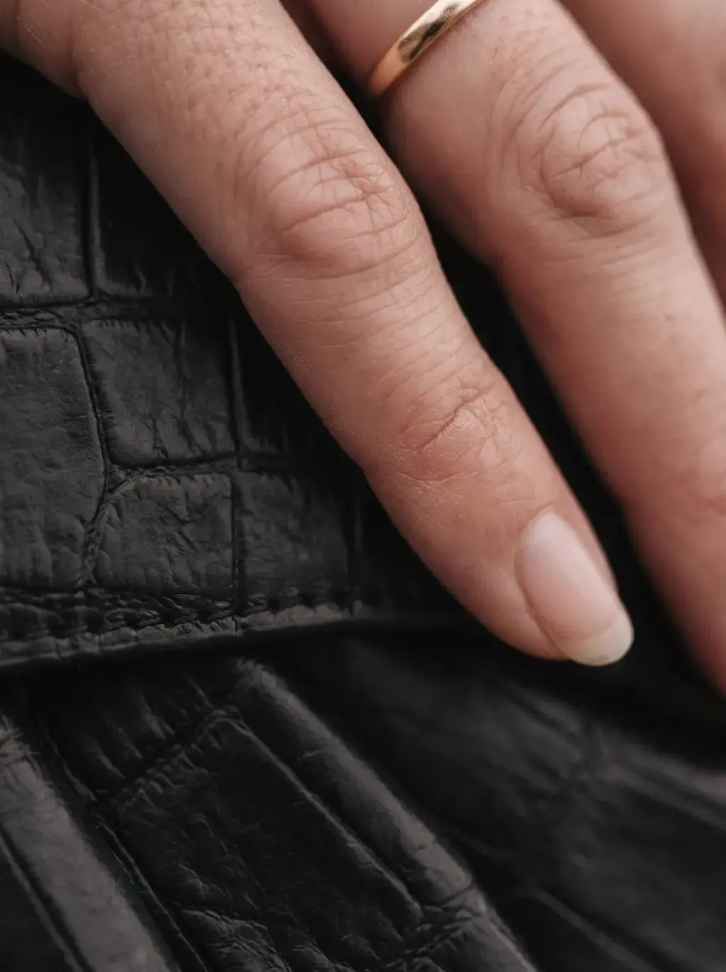 Doigts posés sur les plis souples d’un sac en cuir noir