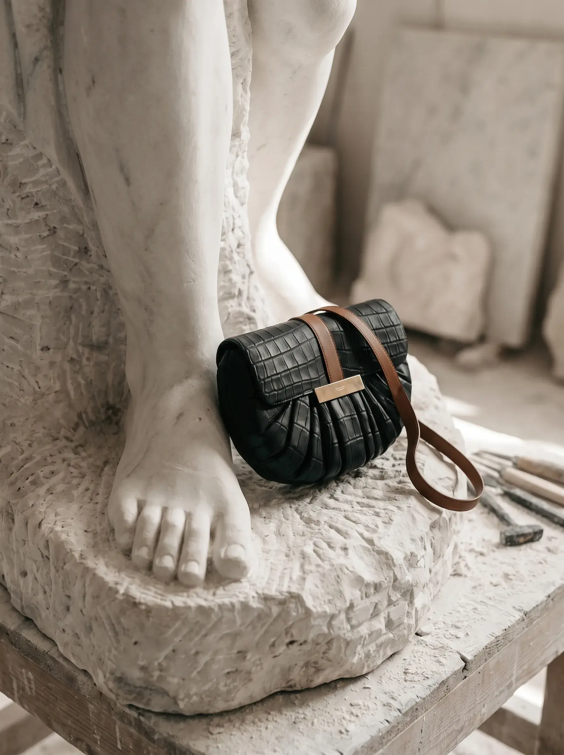 Petit sac noir posé au pied d’une sculpture monumentale en plâtre