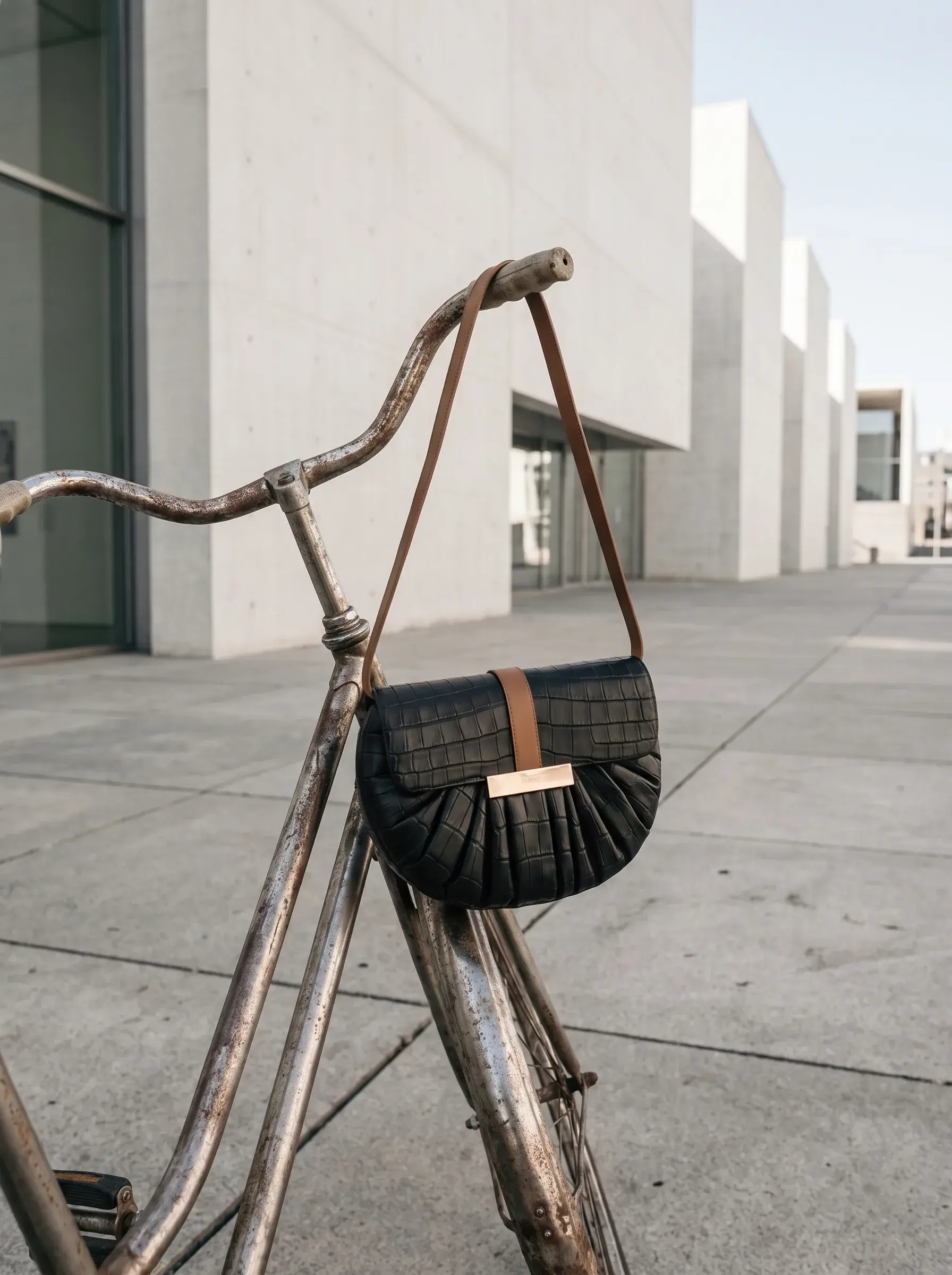 Sac noir suspendu au guidon d’un vélo vintage devant une architecture blanche