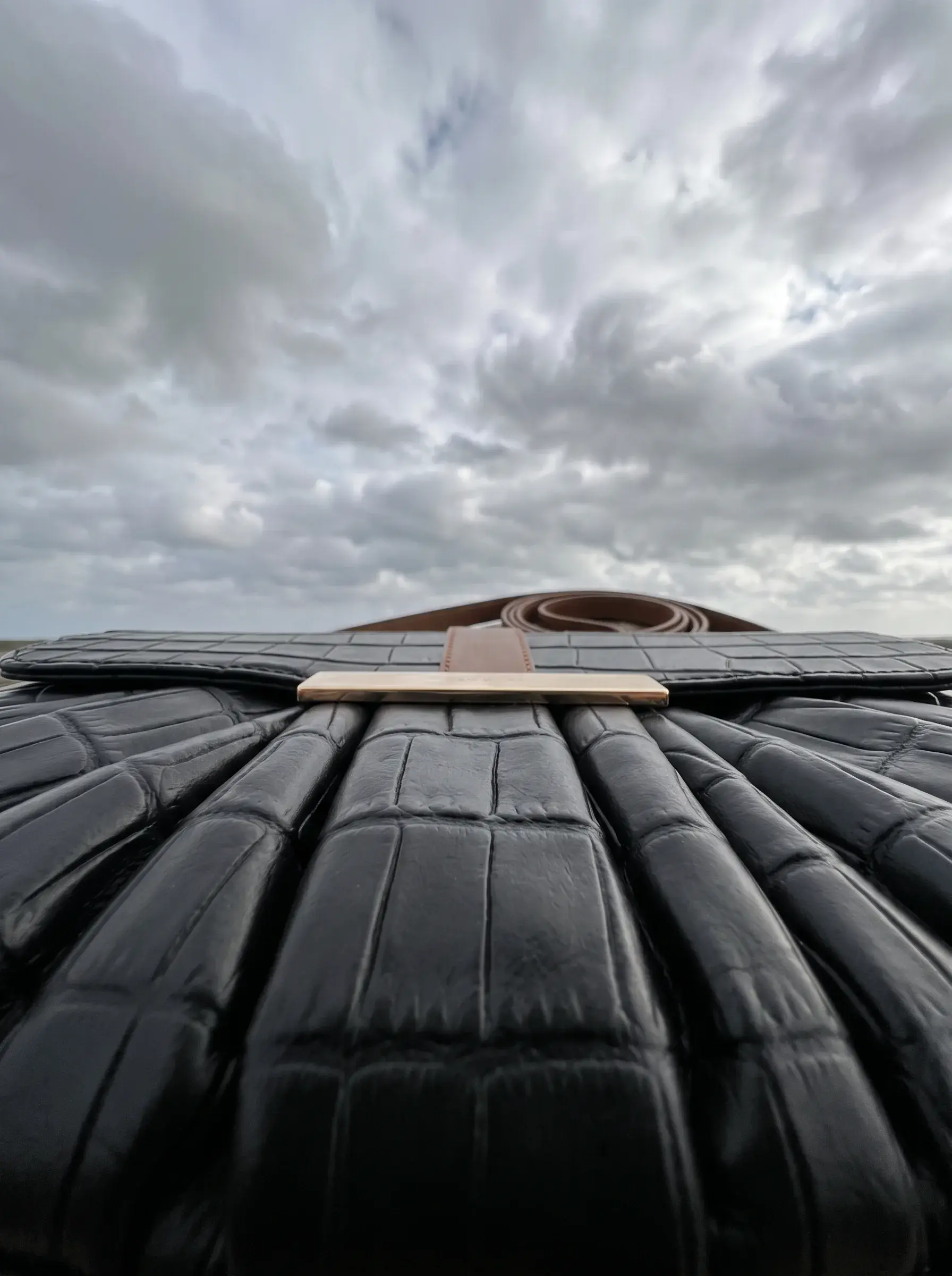 Vue rasante des plis d’un sac noir avec sa sangle brune à l’horizon