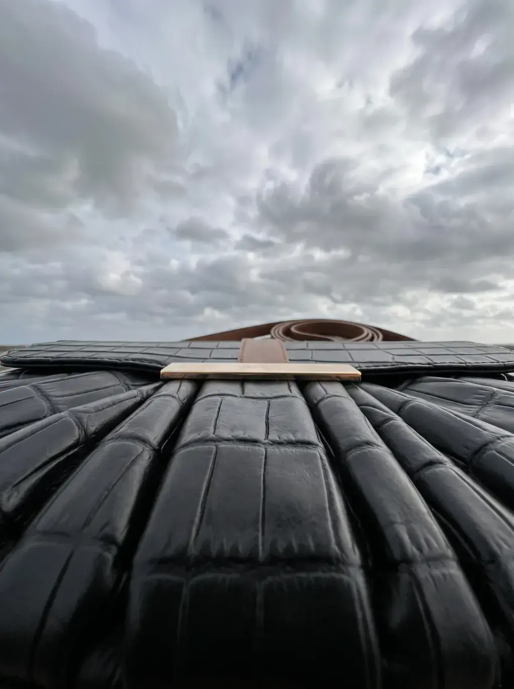 Vue rasante des plis d’un sac noir avec sa sangle brune à l’horizon