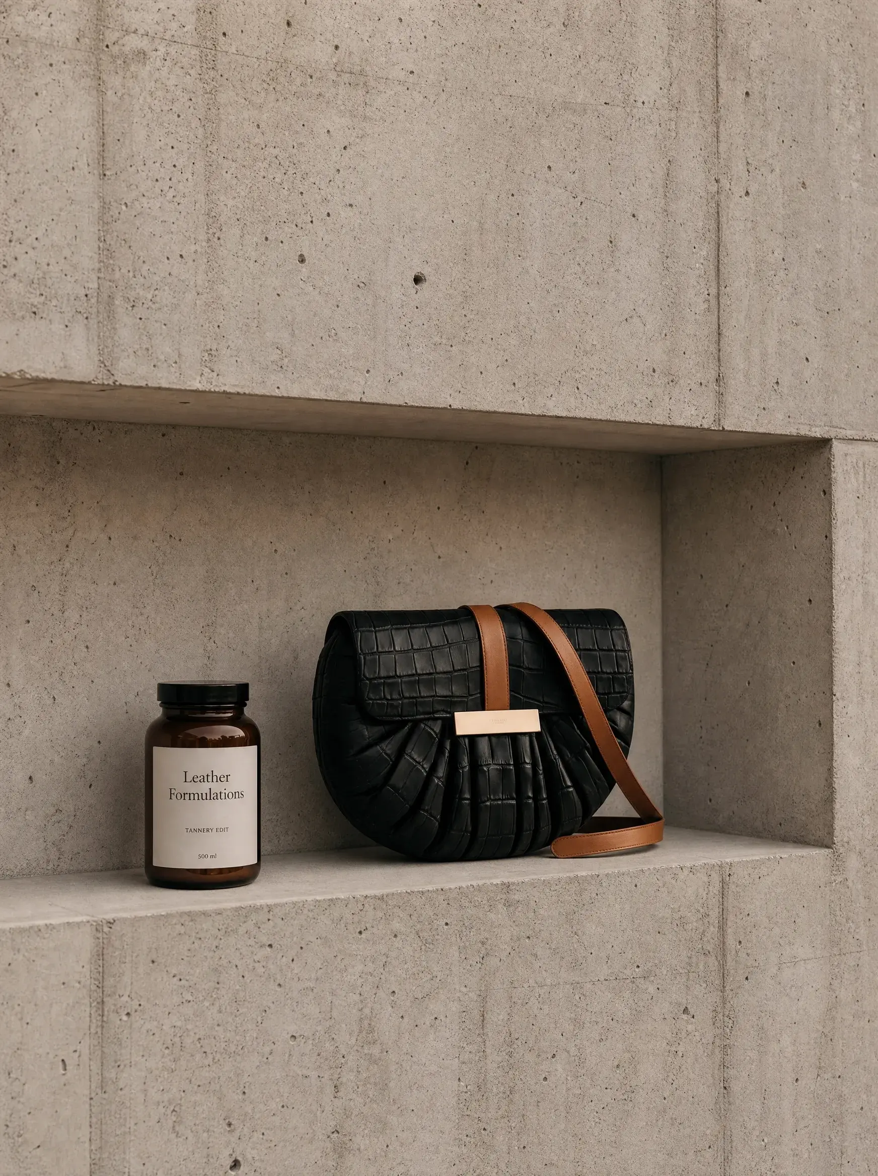Sac noir et flacon brun présentés dans une niche de béton minimaliste
