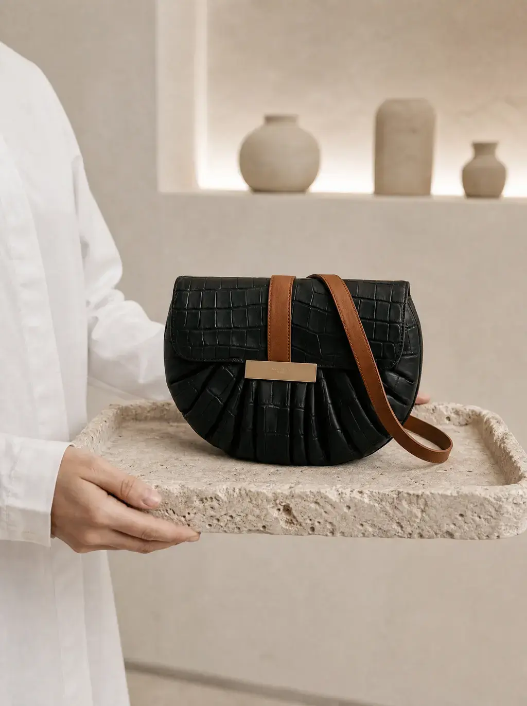 Personne en chemise blanche tenant le sac croco sur plateau, étagères céramiques