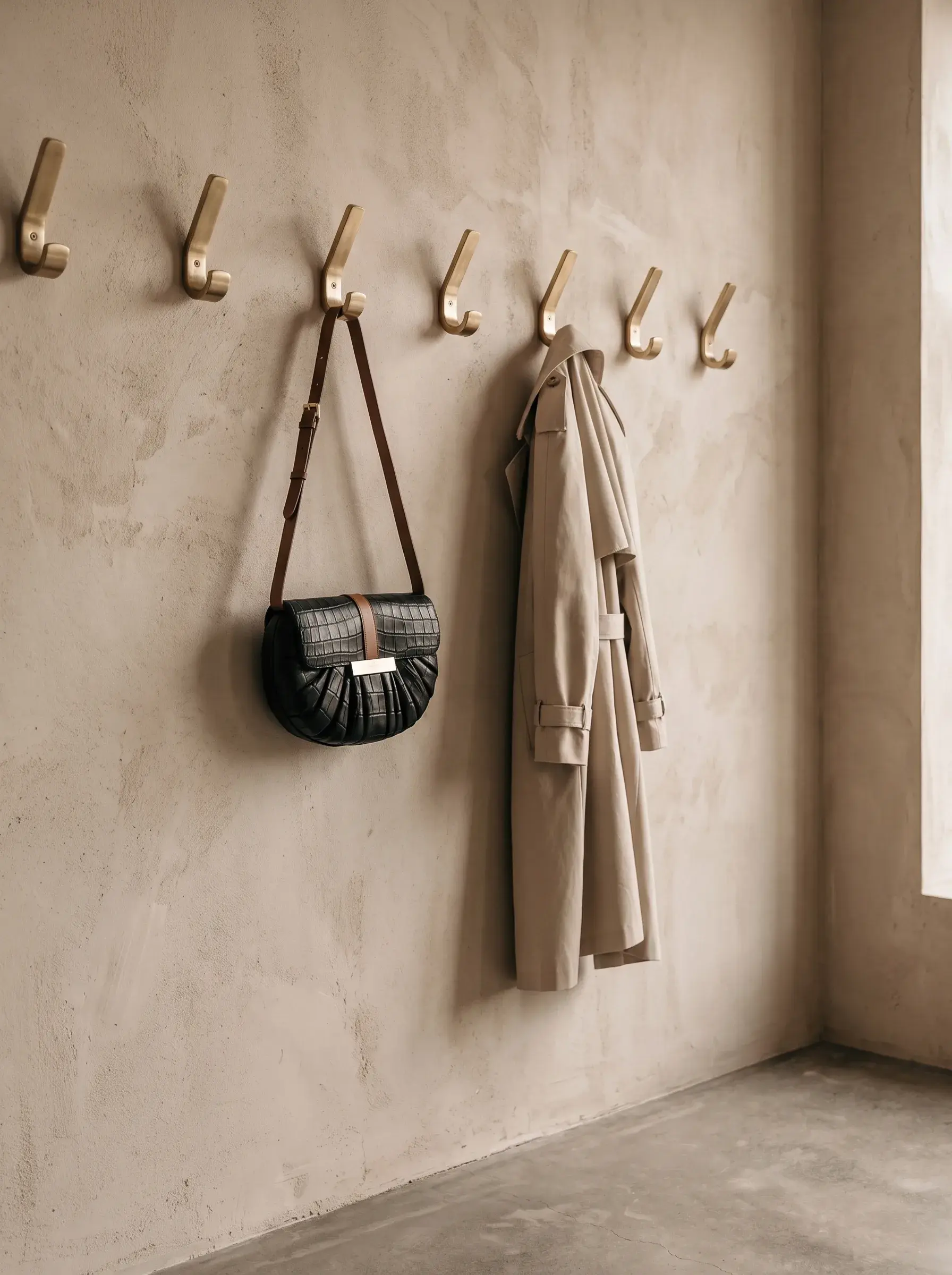 Sac noir et manteau beige suspendus à des patères dans une entrée