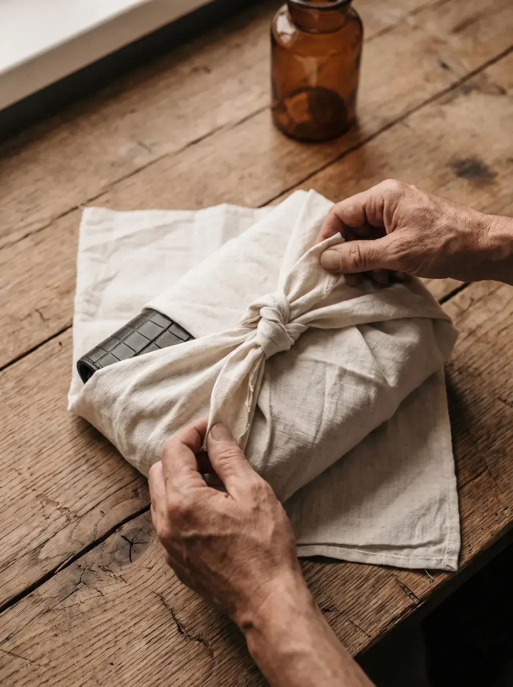 Mains nouant un tissu blanc autour d’un sac pour préparer son emballage