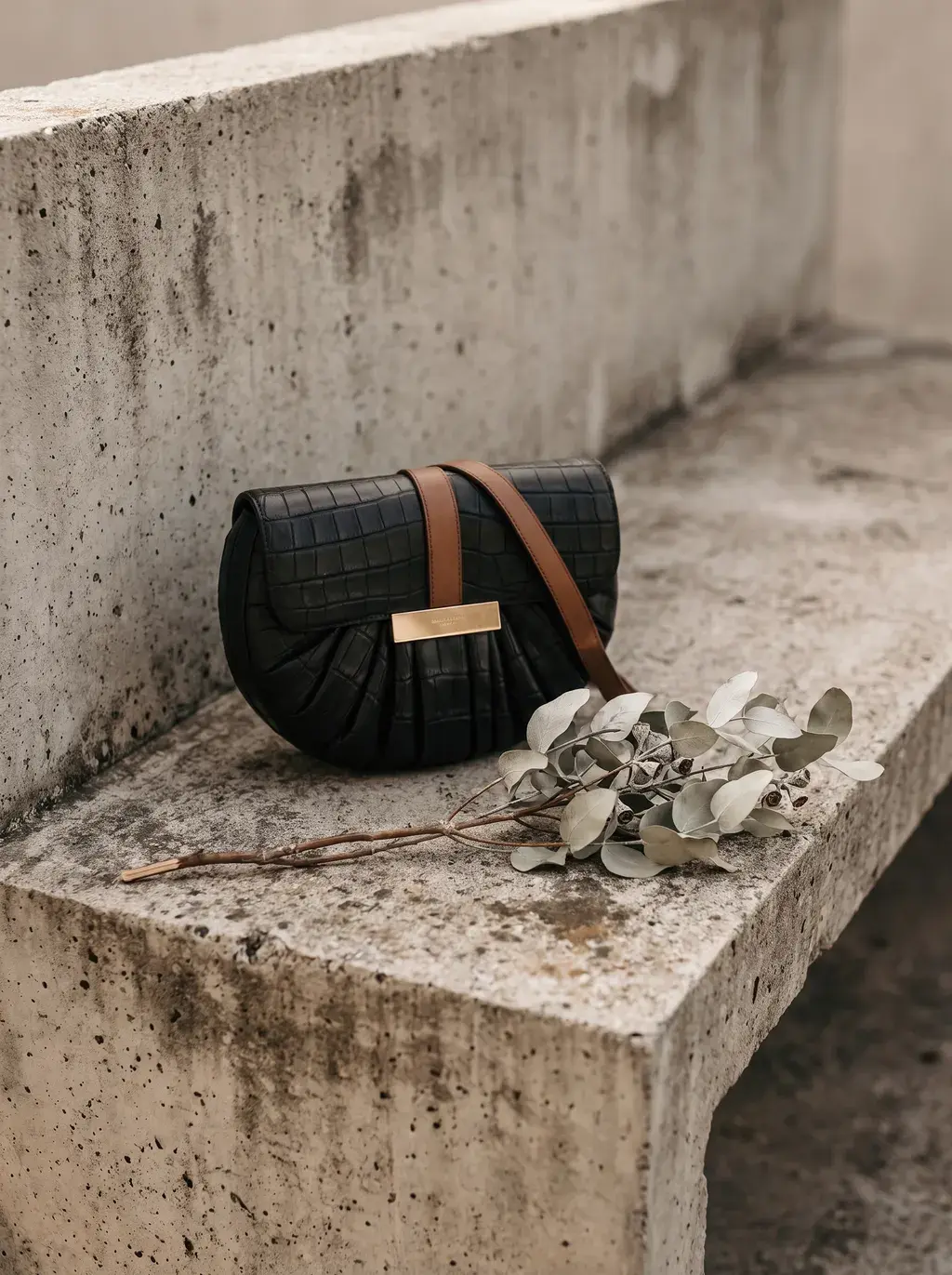 Sac croco sur banc béton avec branche d'eucalyptus, espace urbain extérieur
